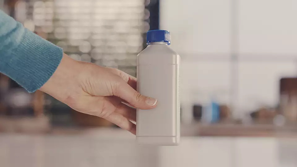 A hand holds a white bottle with a blue cap. The background is blurred.