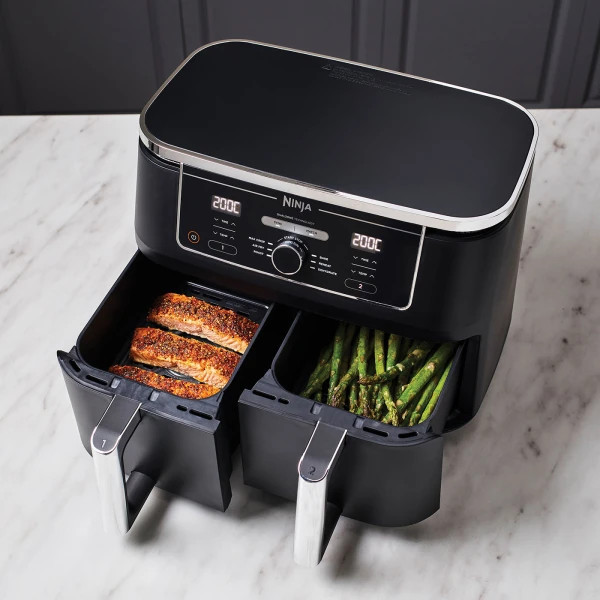 Friteuse à air Ninja noire avec deux compartiments de cuisson, contenant du saumon et des asperges. Affichage numérique.