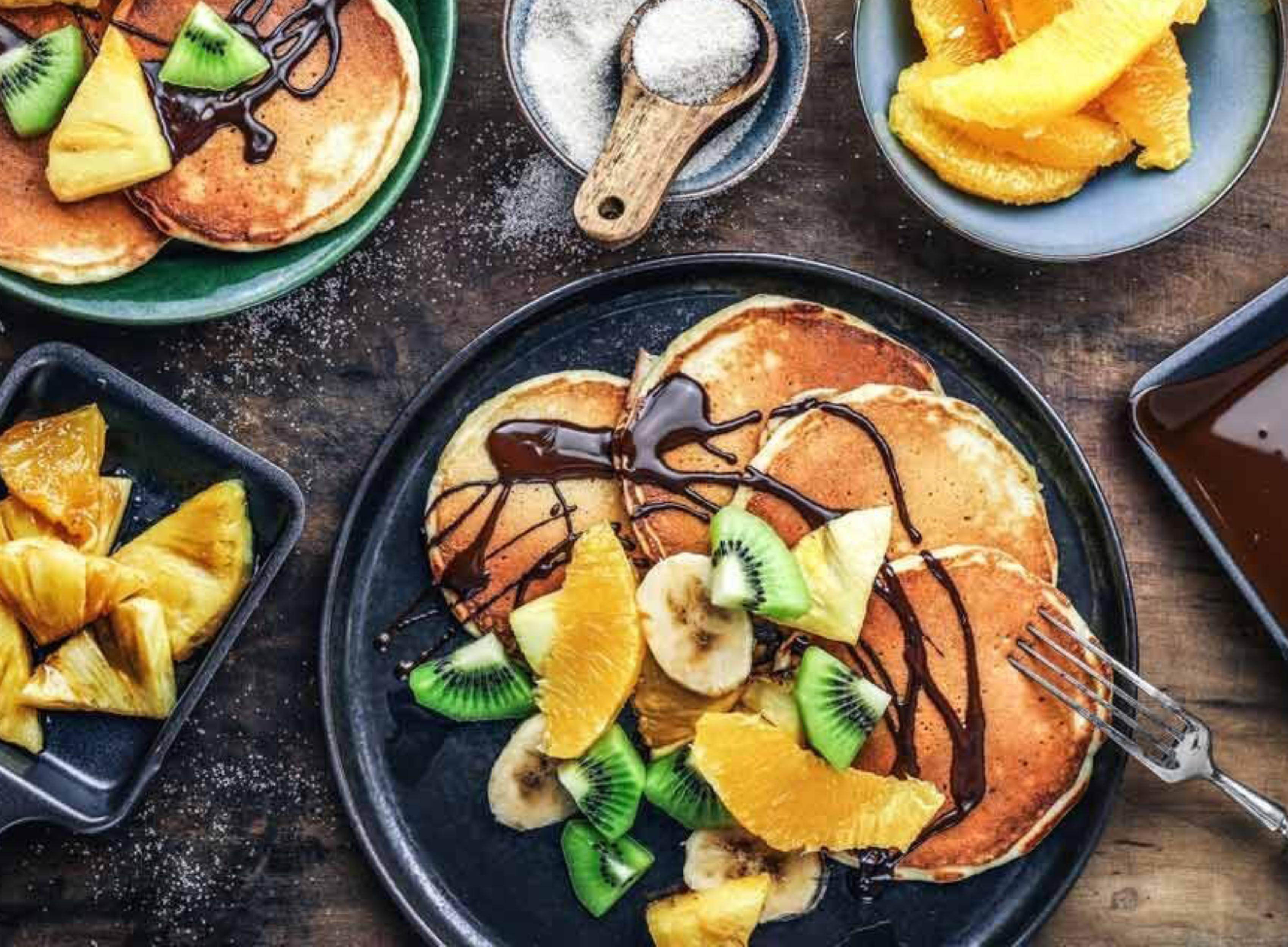 Pfannkuchen mit Obst und Schokoladensauce auf schwarzem Teller, auf Holztisch.