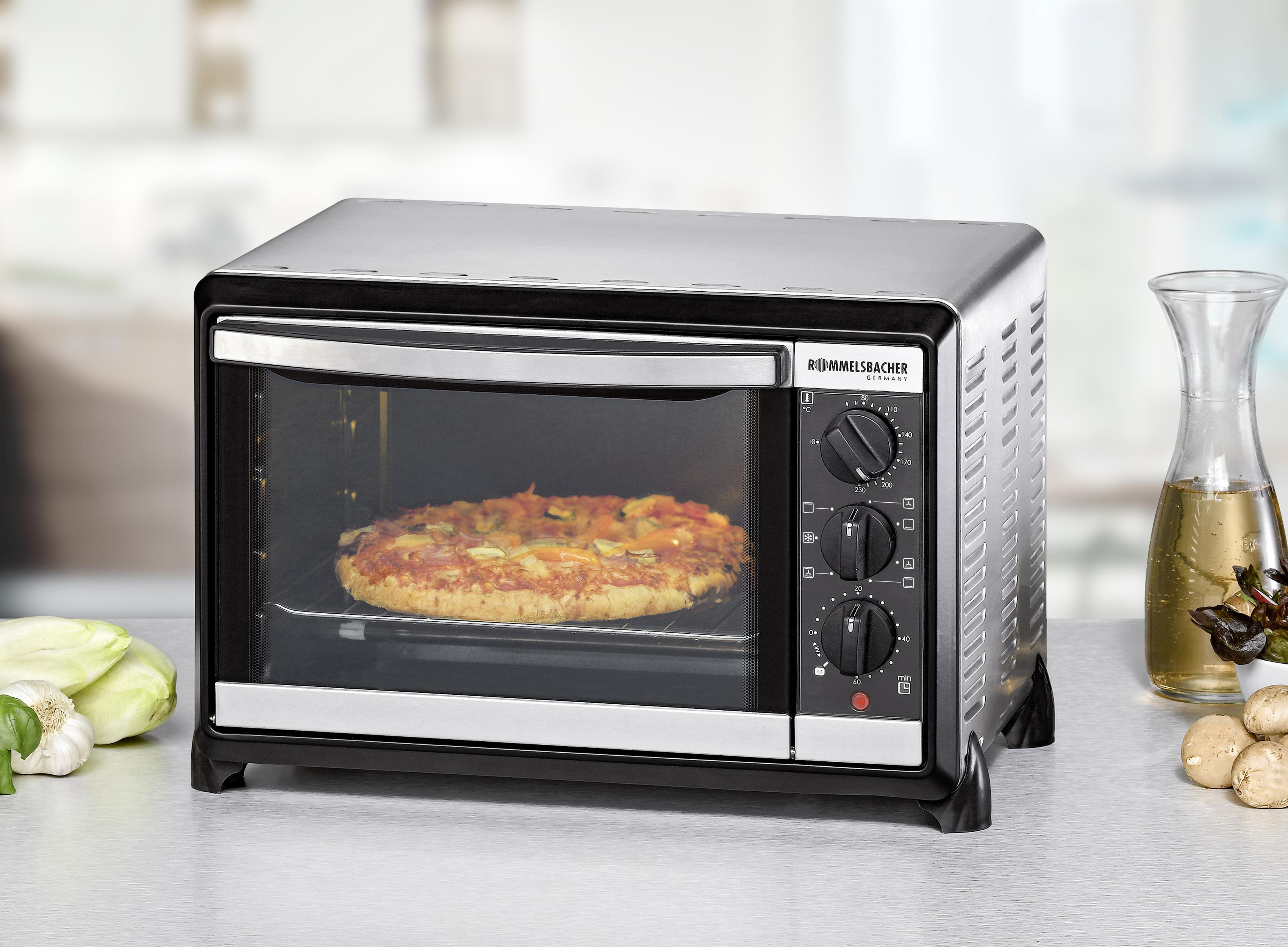 Ein kleiner Tischbackofen mit einer Pizza darin, umgeben von Zutaten.