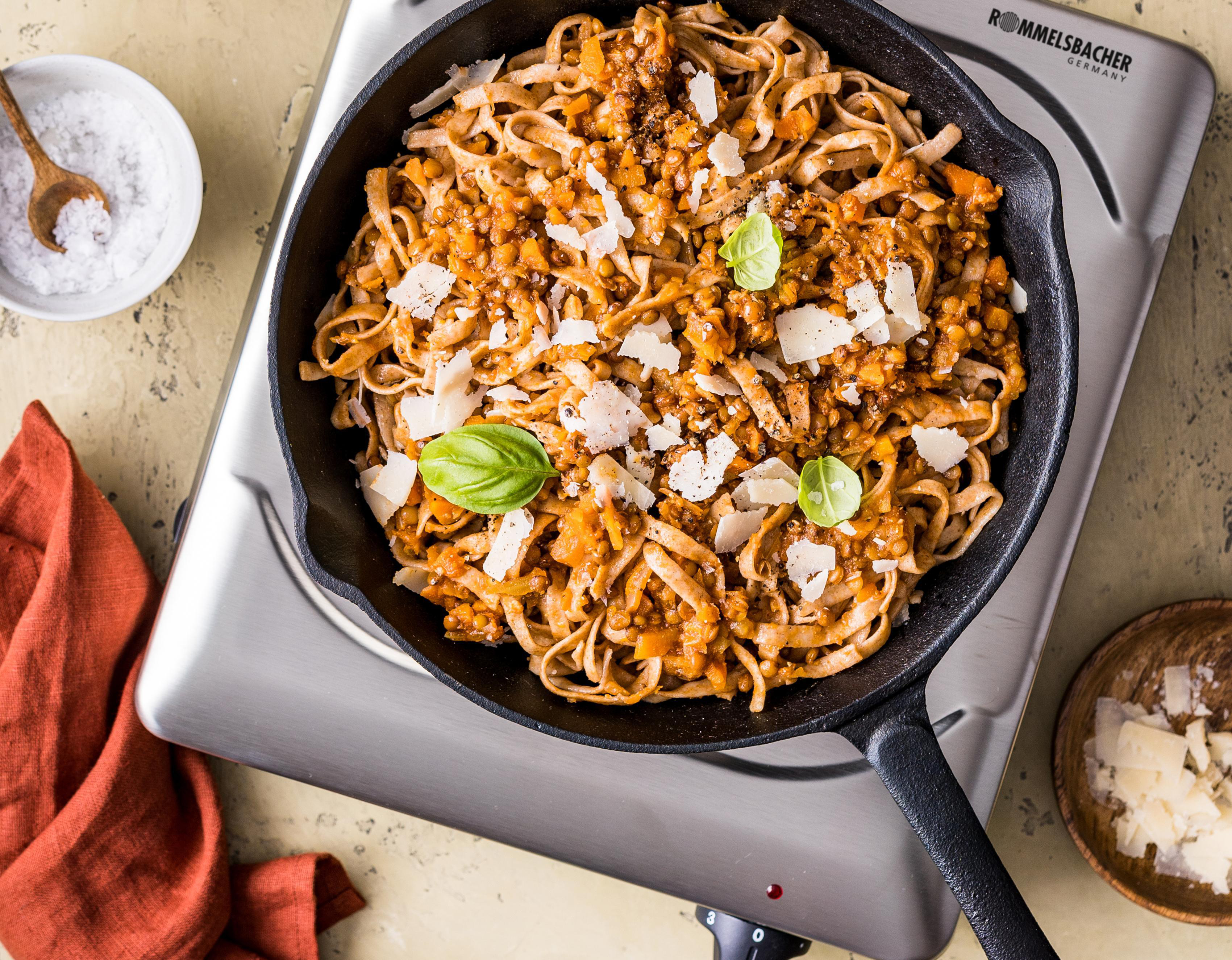 Pastagericht mit Sauce, Käse und Basilikum auf einer Kochplatte.