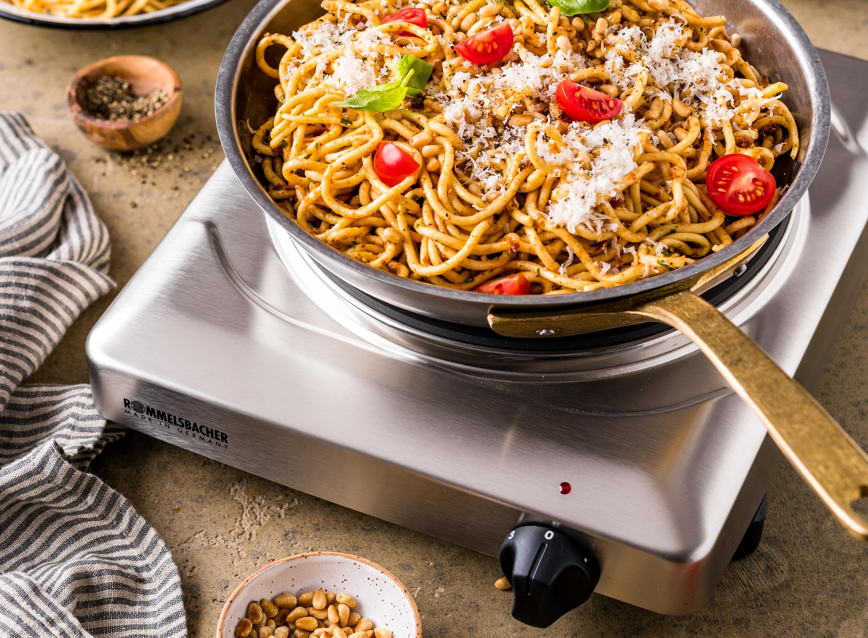 Spaghetti in einer Pfanne auf einer Kochplatte. Tomaten, Käse und Basilikum garnieren das Gericht.