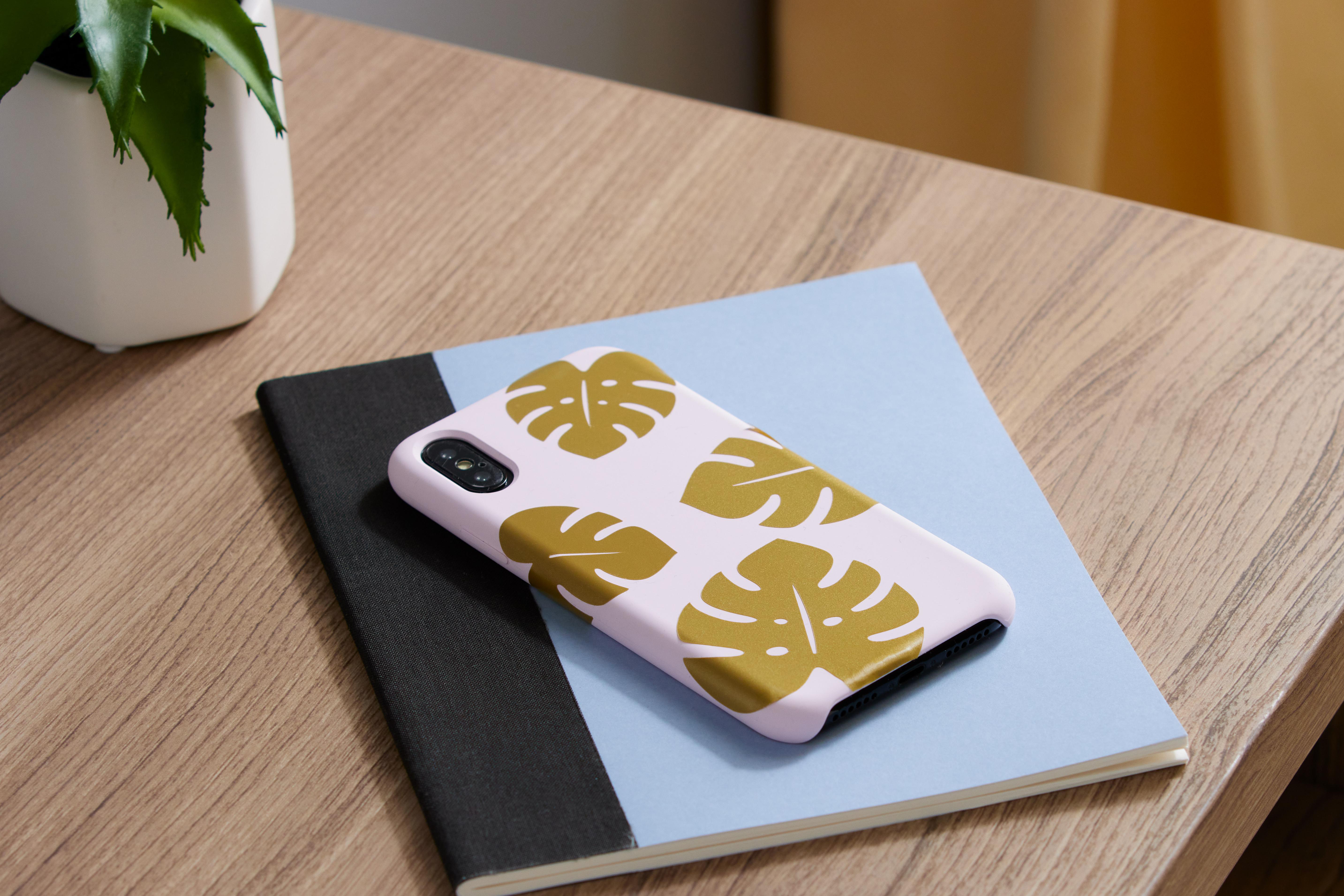 Eine Handyhülle mit hellrosa Hintergrund und goldfarbenem Blattdesign.