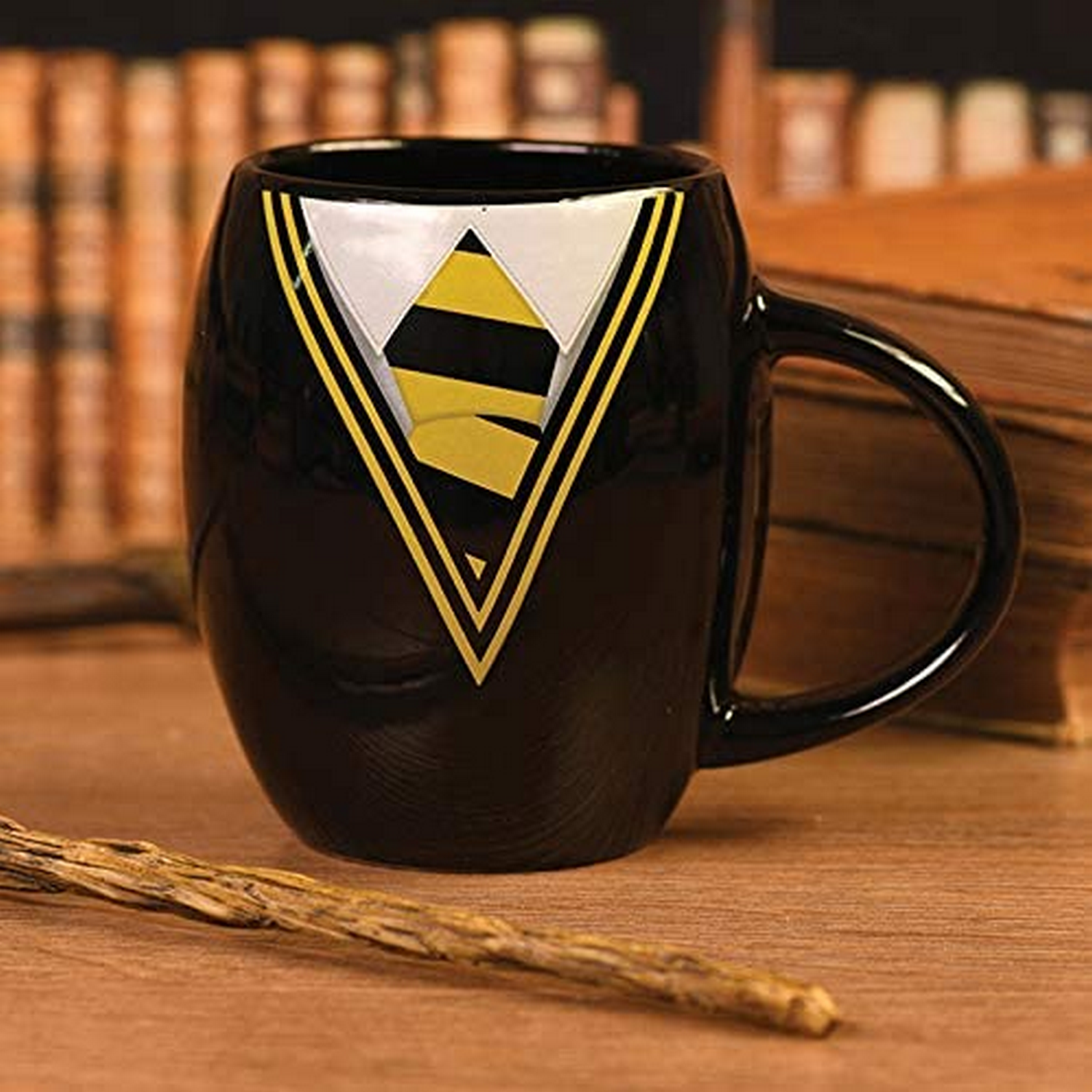 Taza negra con diseño de abrigo amarillo y negro, mesa de madera.