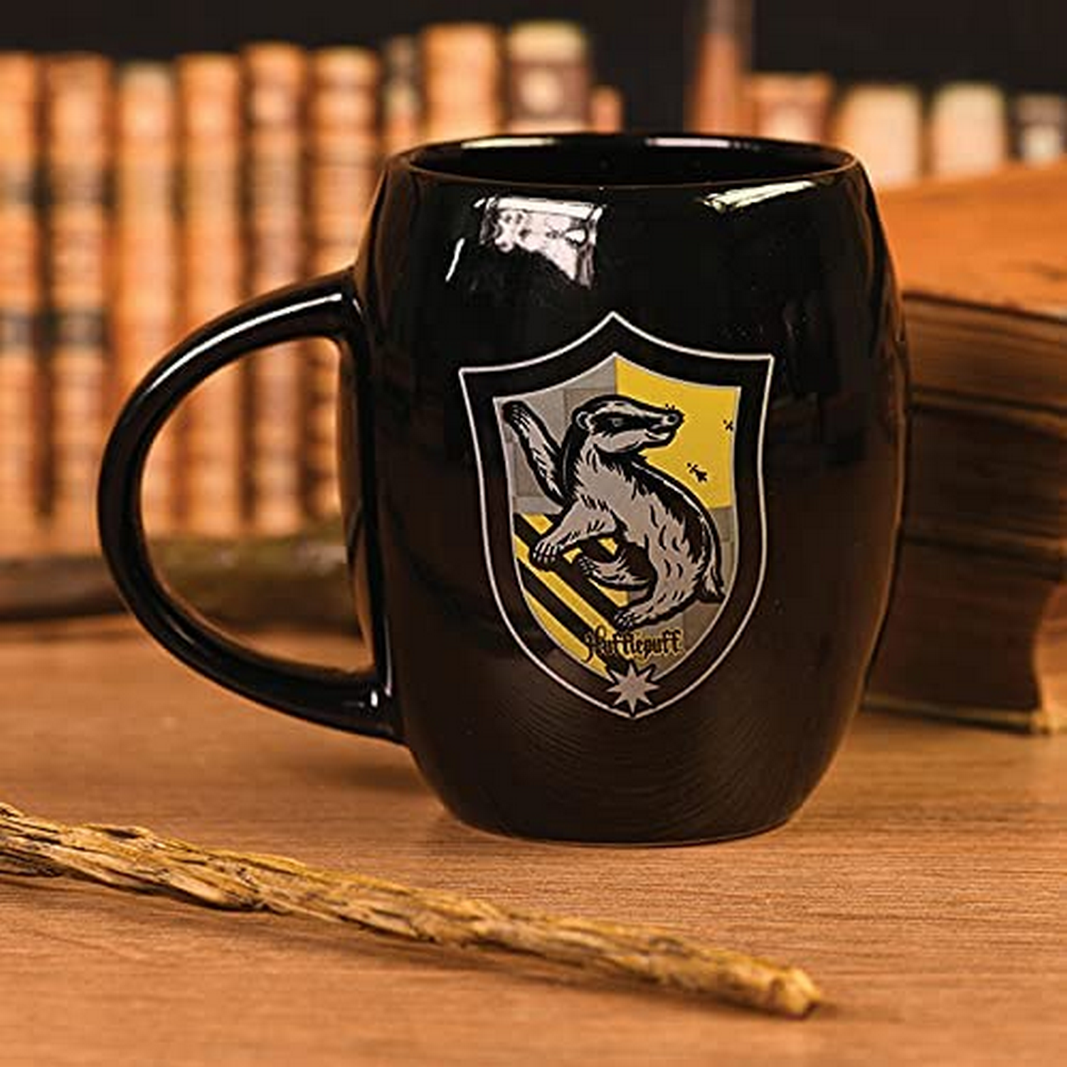 Una taza negra de Hufflepuff con el escudo de la casa. La taza está sobre una superficie de madera con libros en el fondo.
