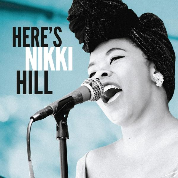 Egy fekete fejkendős nő énekel egy mikrofonba. A háttérben a 'Here's Nikki Hill' szöveg látható.