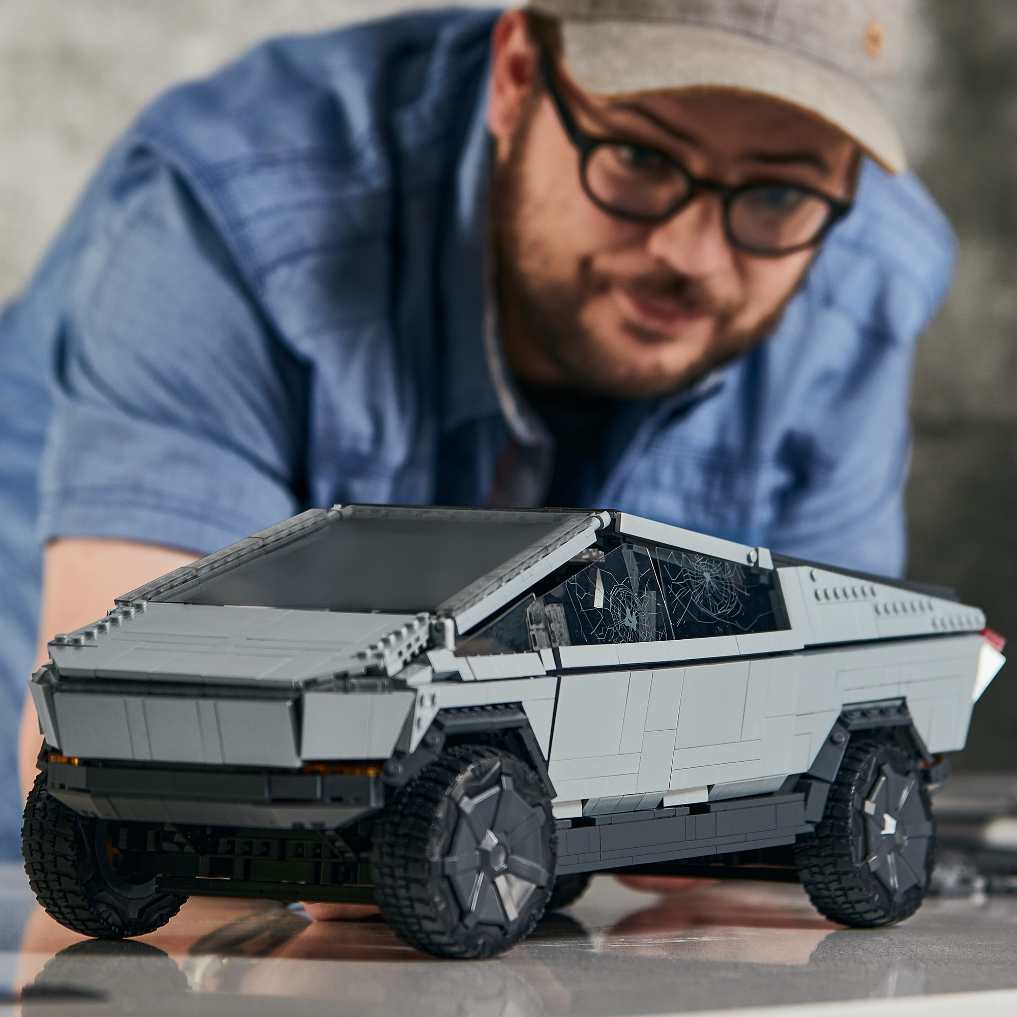 Mann baut graues Cybertruck LEGO-Modell, mit unscharfem Hintergrund und Truck im Fokus.