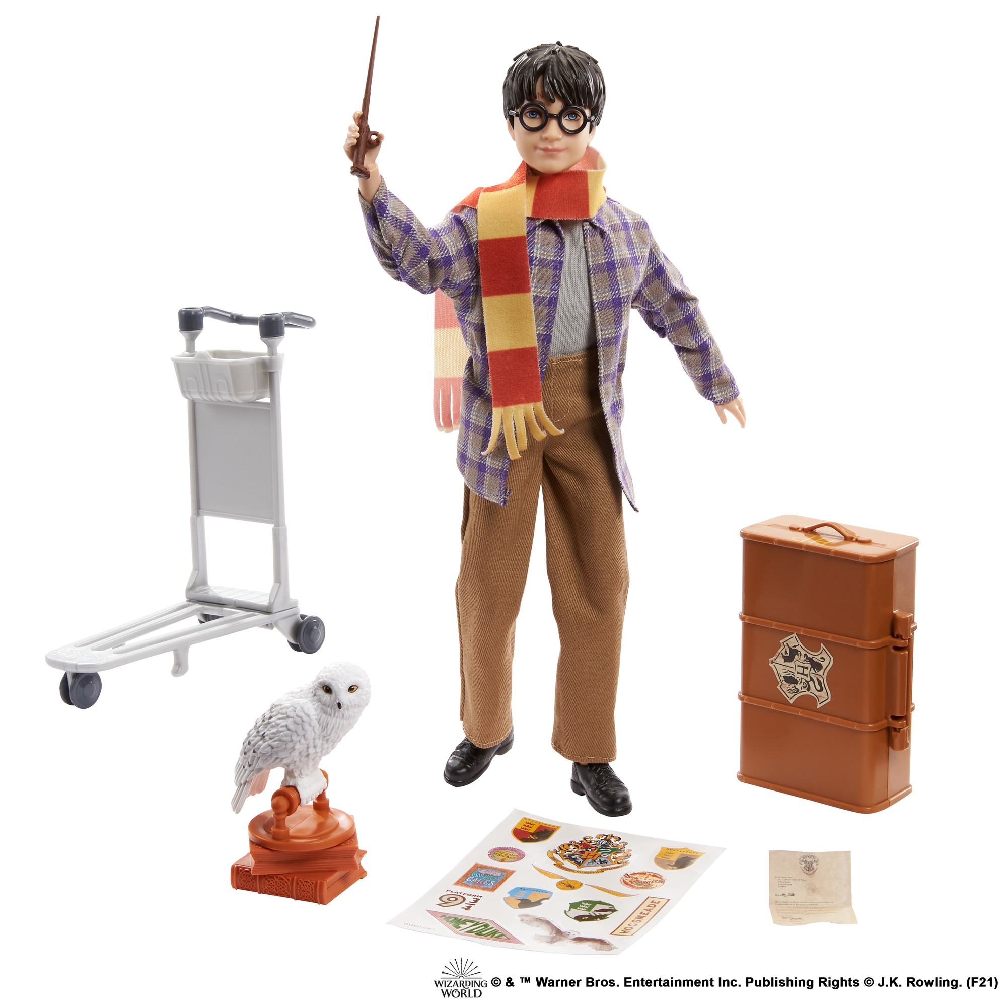 Harry Potter-Puppe mit Zauberstab, Schal, Gepäck, Eule, Gepäckwagen und Aufklebern auf weißem Grund.