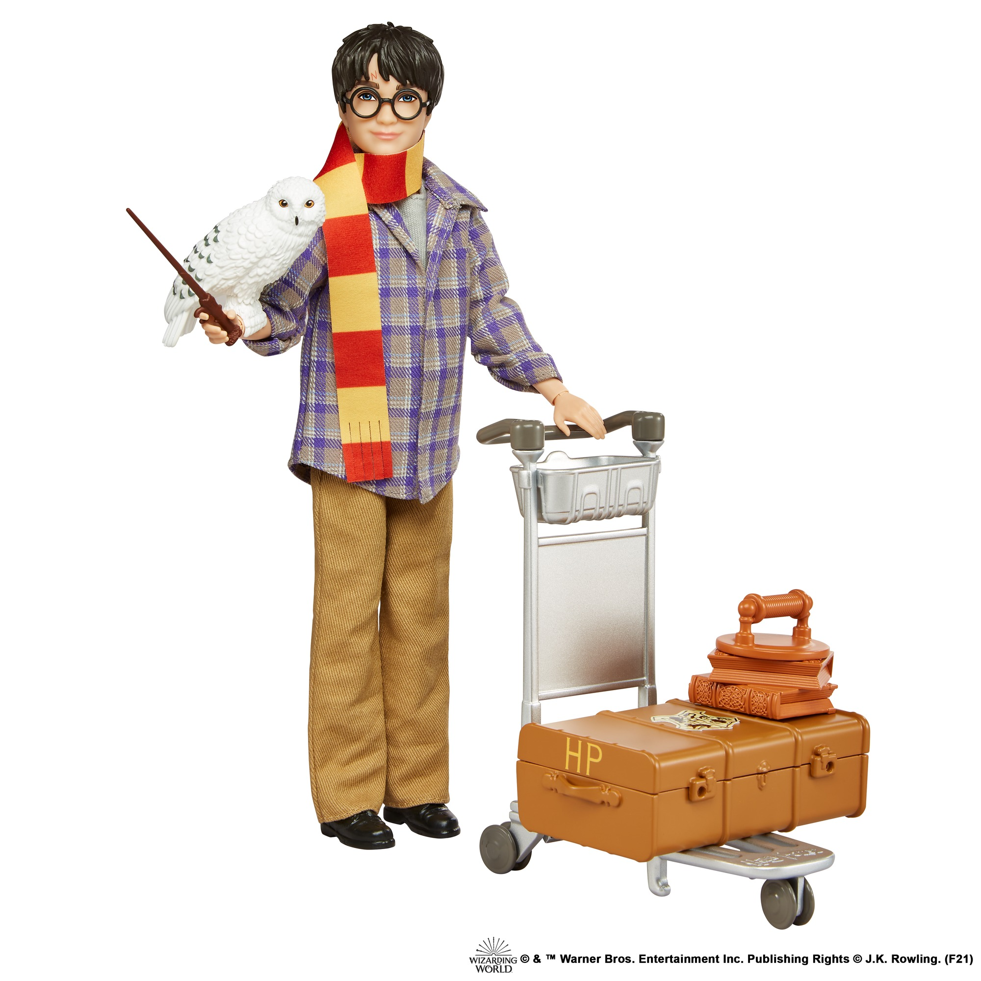 Harry Potter Puppe mit Brille und Schal. Hält einen Zauberstab und eine Eule. Koffer auf einem Gepäckwagen. Weißer Hintergrund.