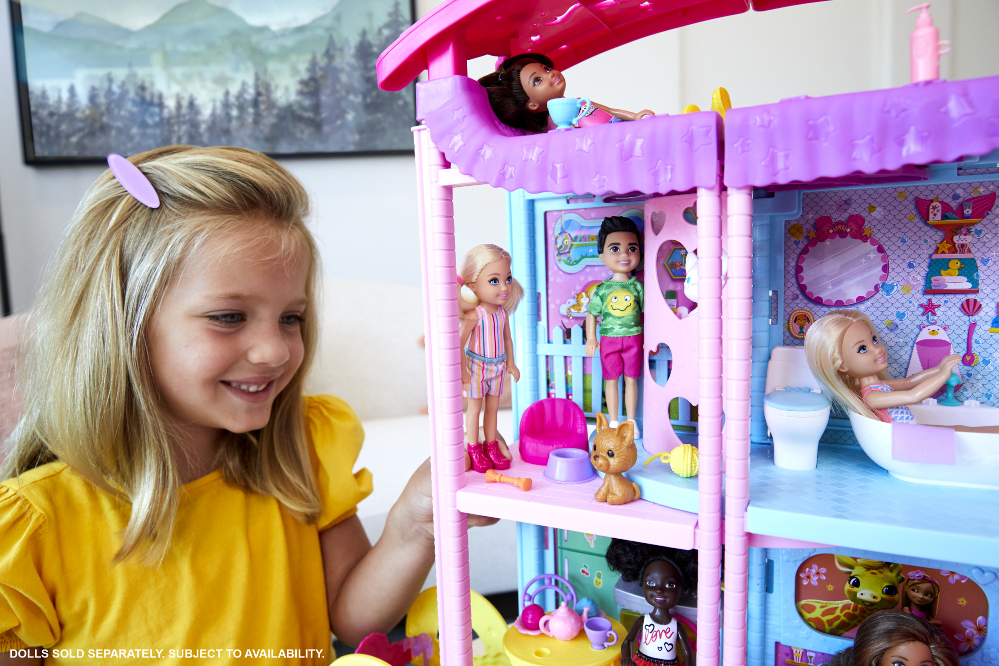 Ein Mädchen lächelt und spielt mit einem Puppenhaus mit Puppen und Miniaturmöbeln.