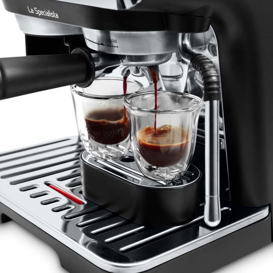 Machine à expresso versant du café dans deux tasses en verre sur une base en acier inoxydable.