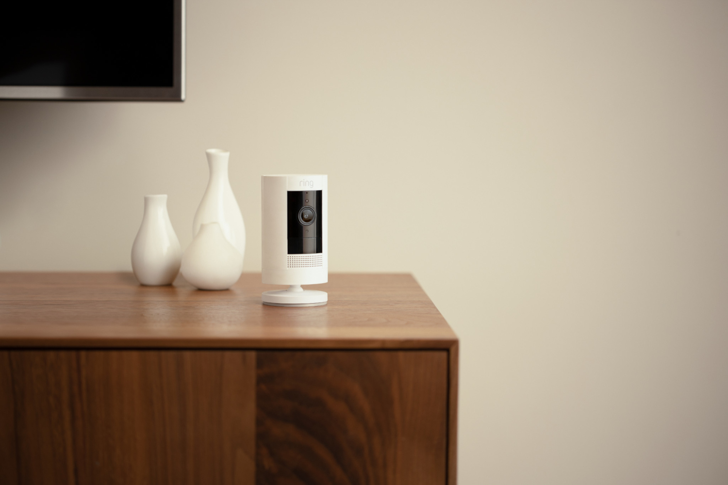Caméra de sécurité Ring blanche sur une surface en bois. Deux vases blancs derrière, mur beige.