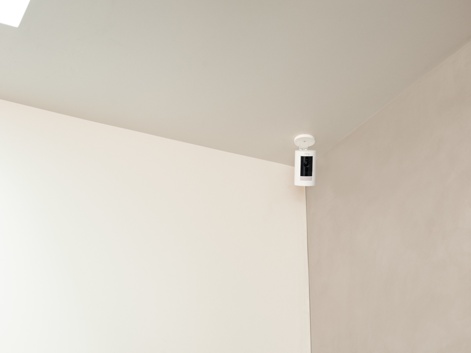Caméra de sécurité Ring blanche montée sur un coin de plafond, murs crème et blancs.