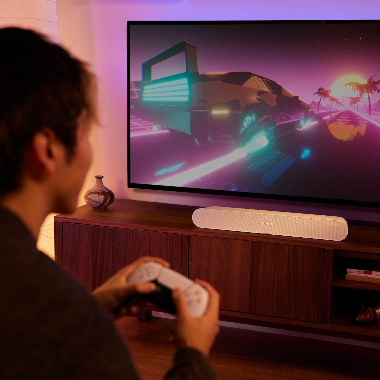 Een persoon houdt een witte gamecontroller vast en kijkt naar een tv-scherm met een nachtelijke stadsscène.