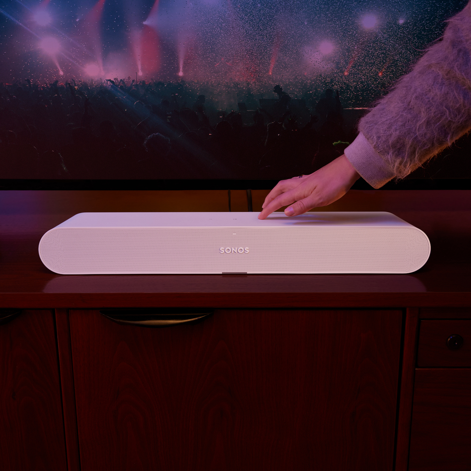 Witte Sonos soundbar op een houten kast, met een hand die hem aanraakt.