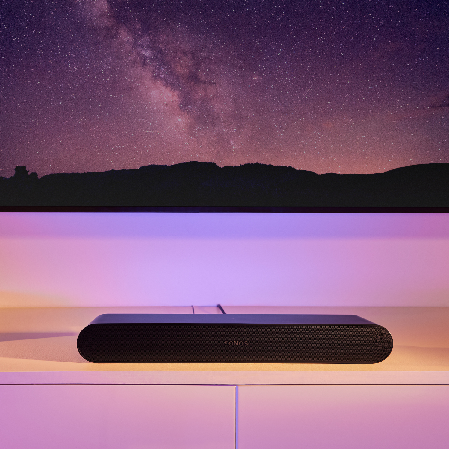 Zwarte Sonos soundbar onder een tv. Achtergrond toont een sterrenhemel en paarse verlichting.