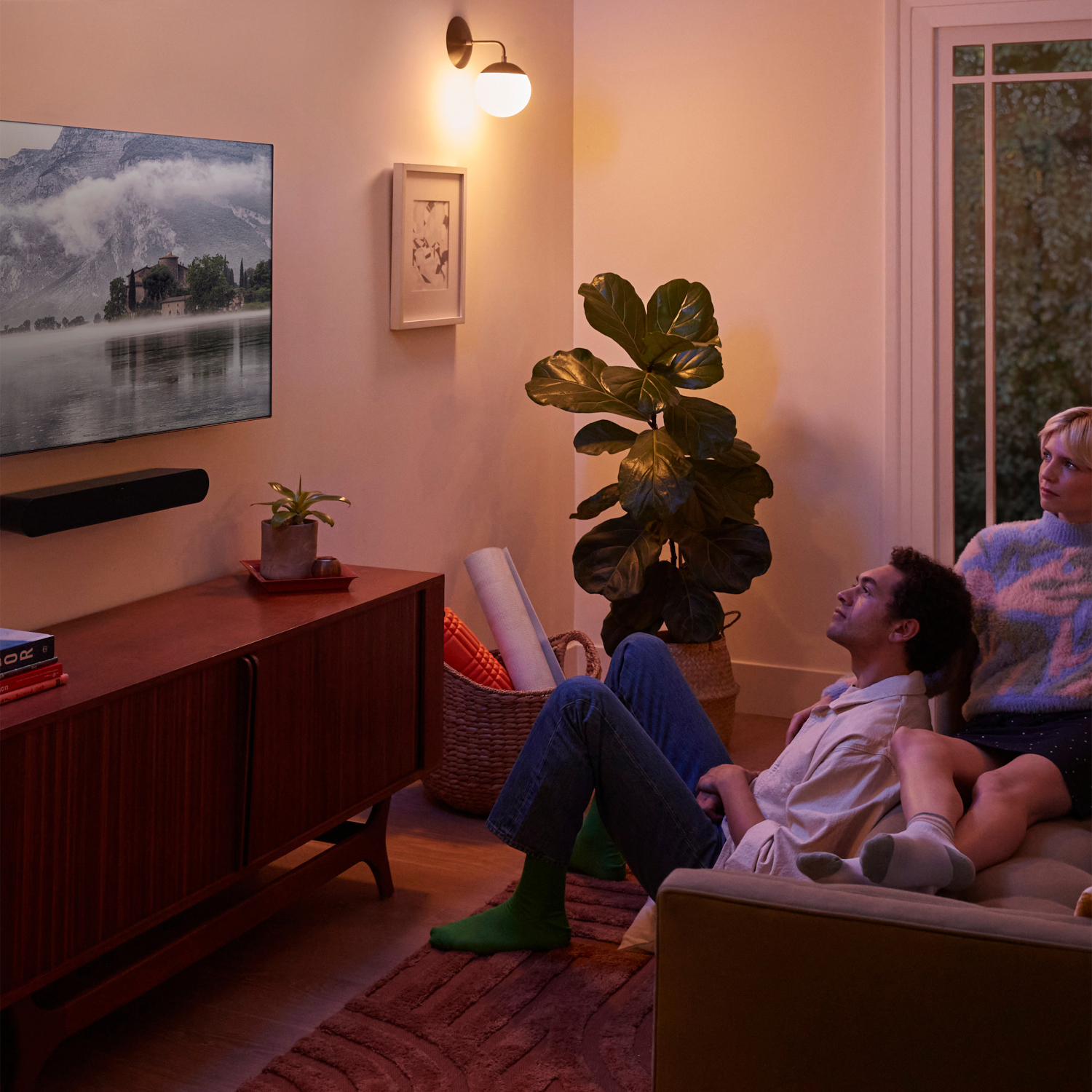 Twee mensen op een bank kijken tv. Een berglandschap staat op het scherm.