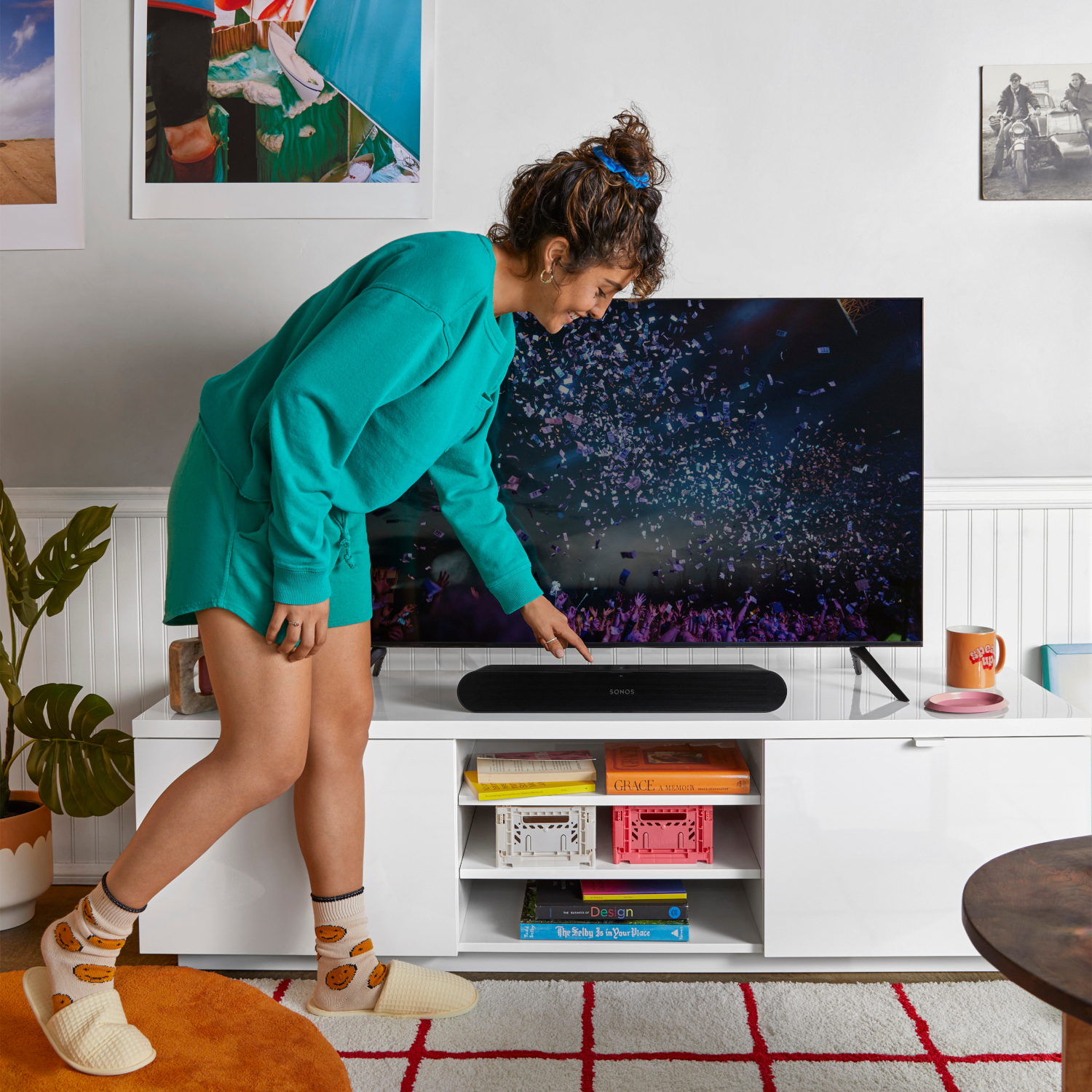 Vrouw wijst naar soundbar op witte kast. TV met confetti op de achtergrond.