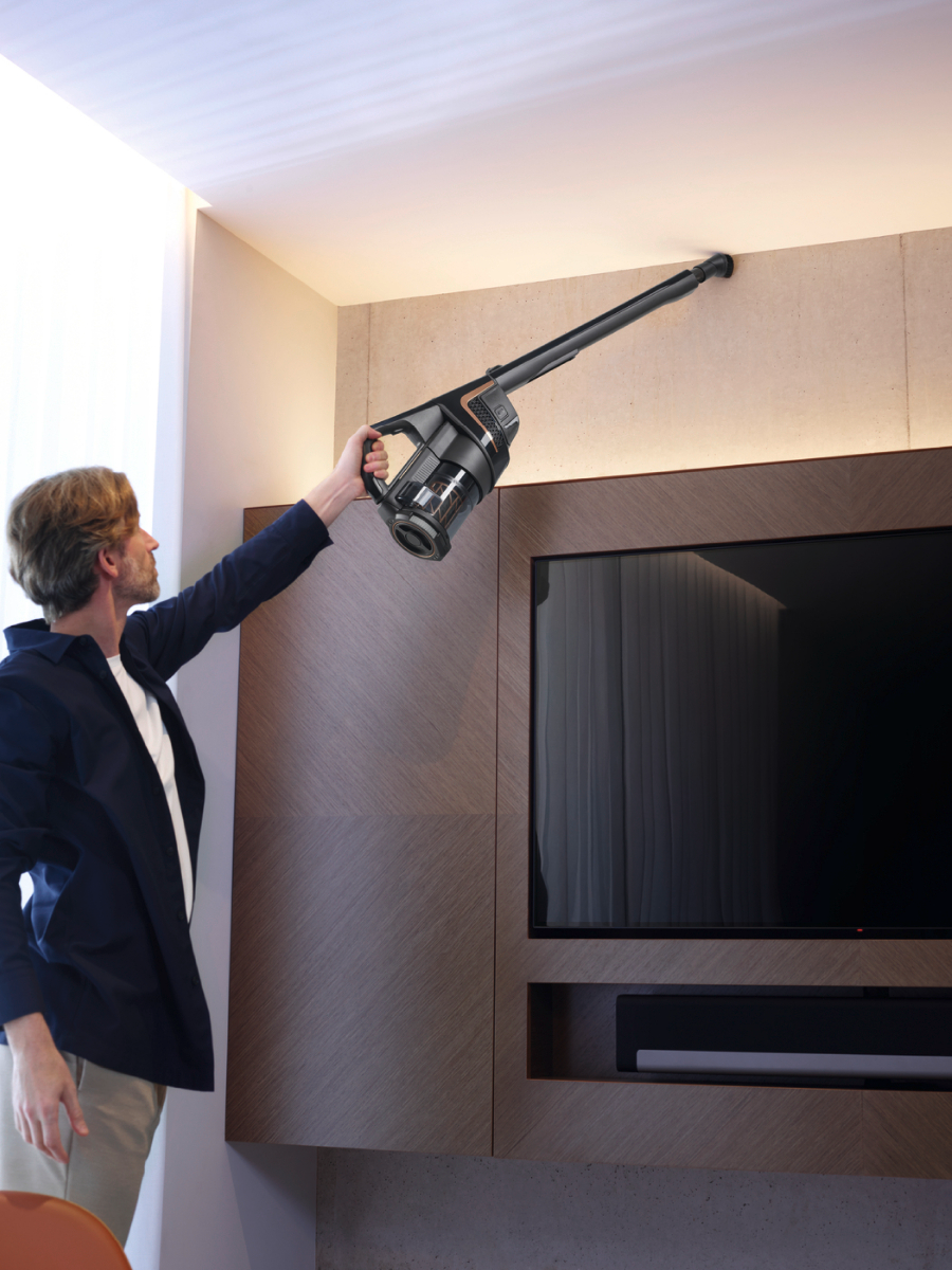 Un uomo aspira un angolo del soffitto con un aspirapolvere nero, in una stanza moderna.