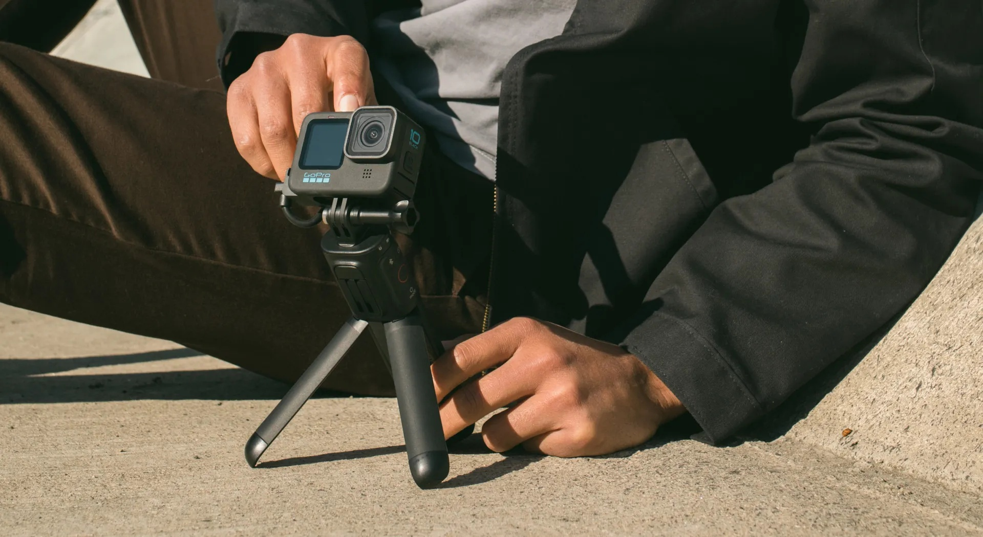 Eine Person sitzt am Boden und hält eine schwarze GoPro-Kamera mit Stativ.