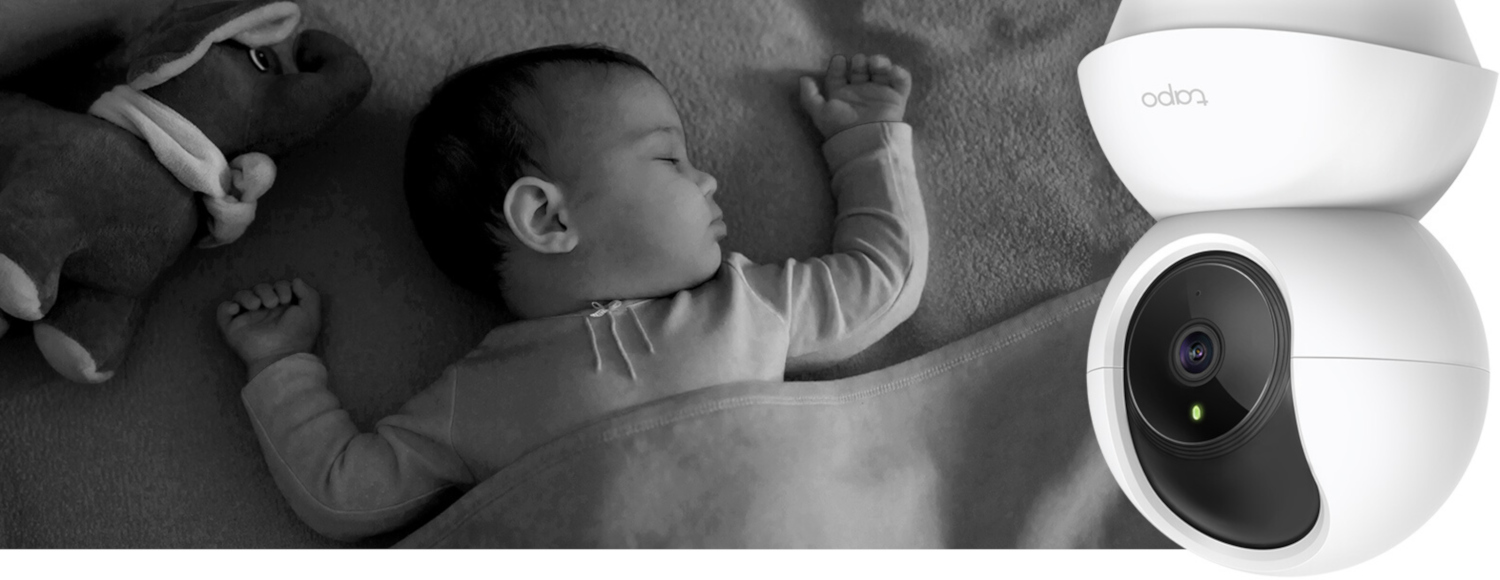 Baby slaapt onder een deken naast een witte Tapo camera, zwart-wit afbeelding.