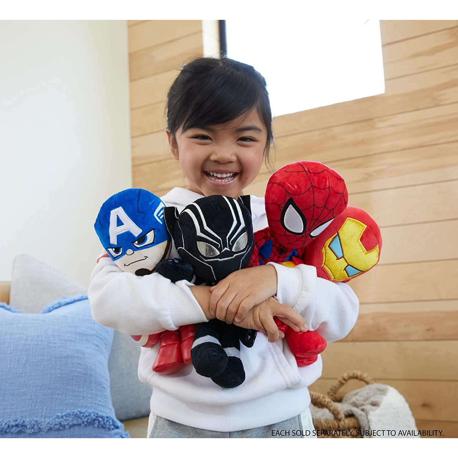 Un niño sonriente sostiene peluches de superhéroes: Capitán América, Pantera Negra, Spider-Man e Iron Man.