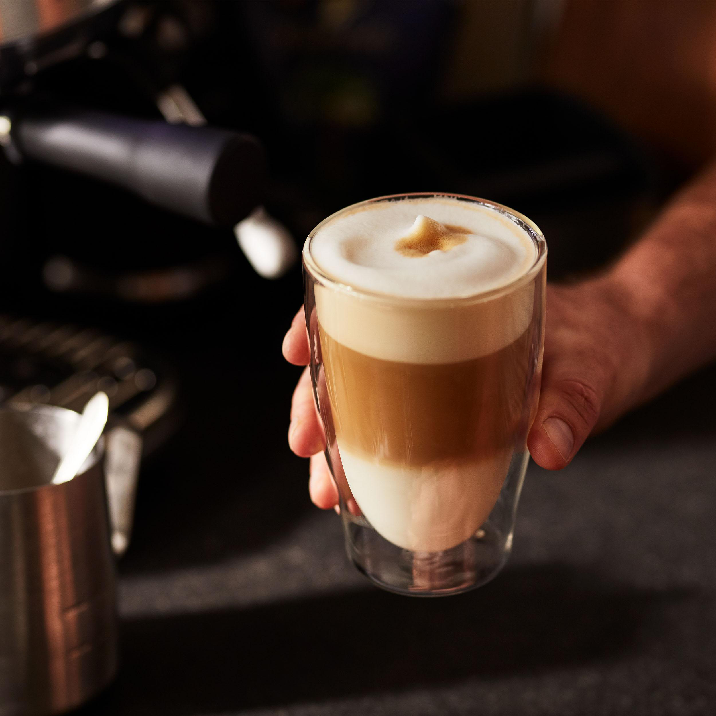 Ein geschichtetes Latte-Glas, das von einer Person gehalten wird; schwarzer Hintergrund.