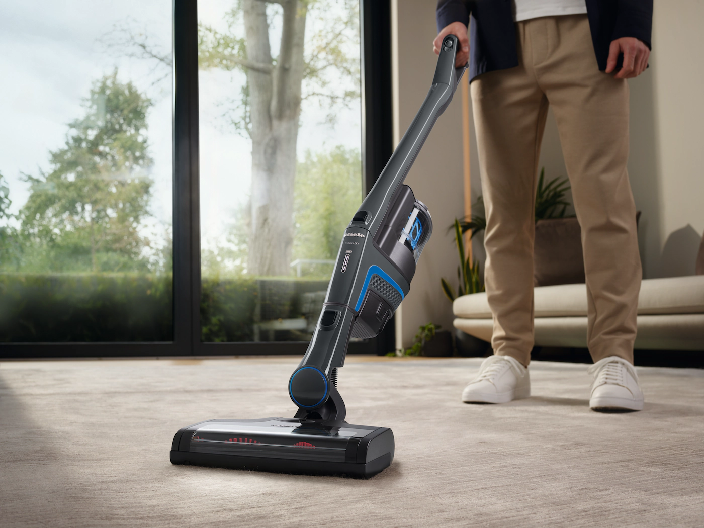 Homme passant l'aspirateur sur un tapis avec un aspirateur sans fil. Montre l'aspirateur et les jambes de l'homme.