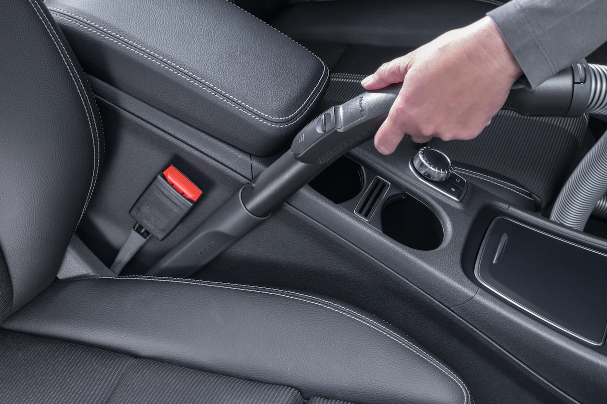Eine Person, die einen Autoinnenraum saugt, mit Fokus auf den Sitz und den Mittelkonsolenbereich.