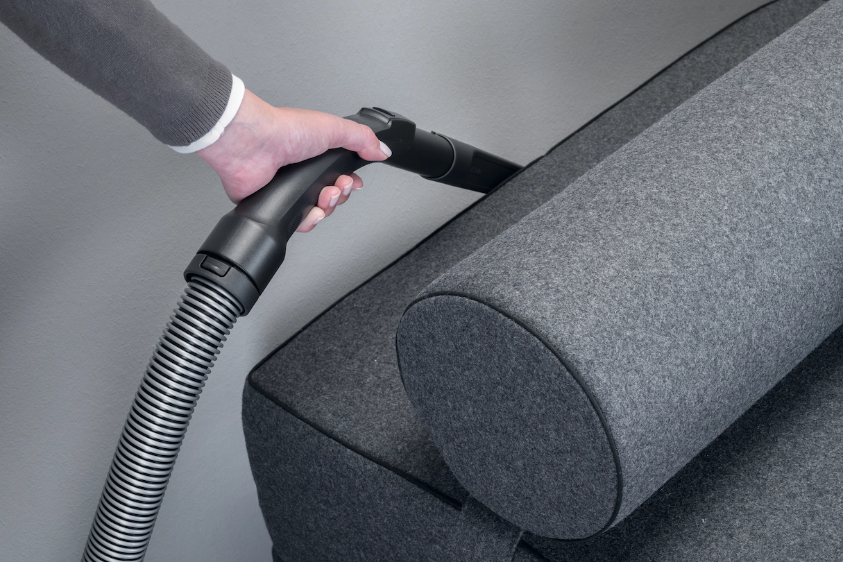 Person saugt ein graues Sofa mit einem Handstaubsauger ab.