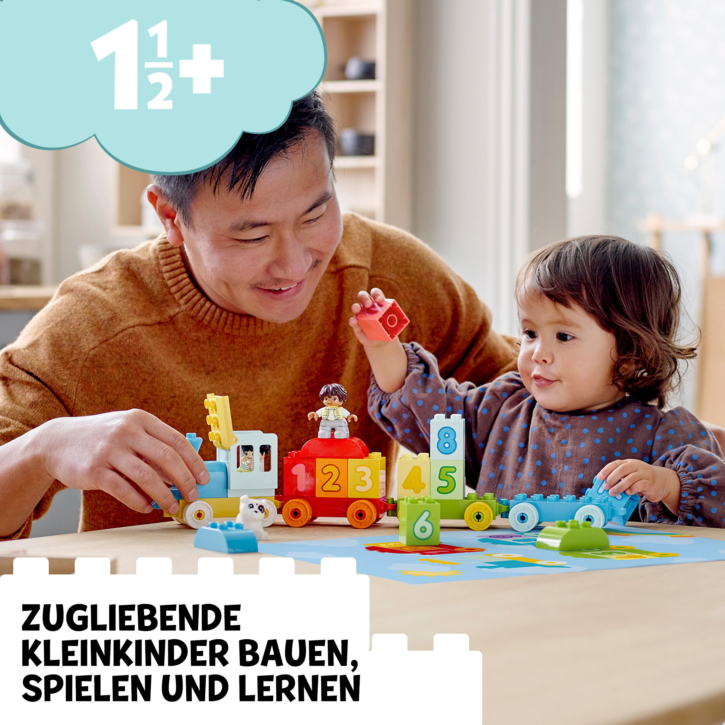 Ein Mann und ein Kind spielen mit Spielzeugzügen. Die Züge sind bunt und auf einer Spielmatte.