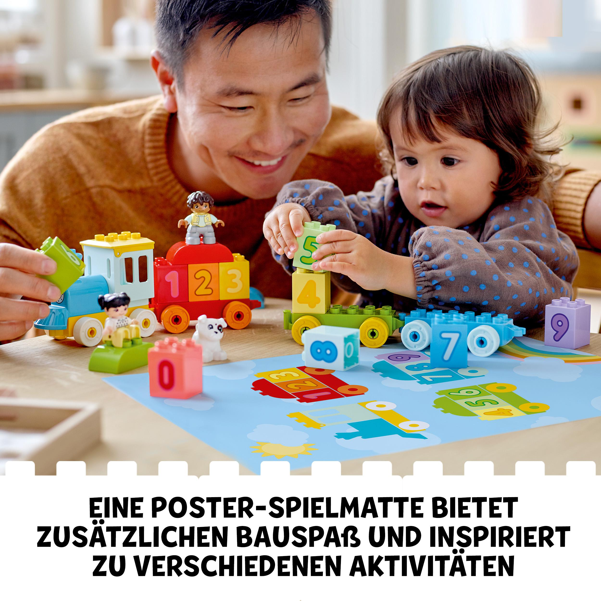 Vater und Kind spielen mit einer Spielzeugeisenbahn und Blöcken auf einer blauen Matte mit Text.