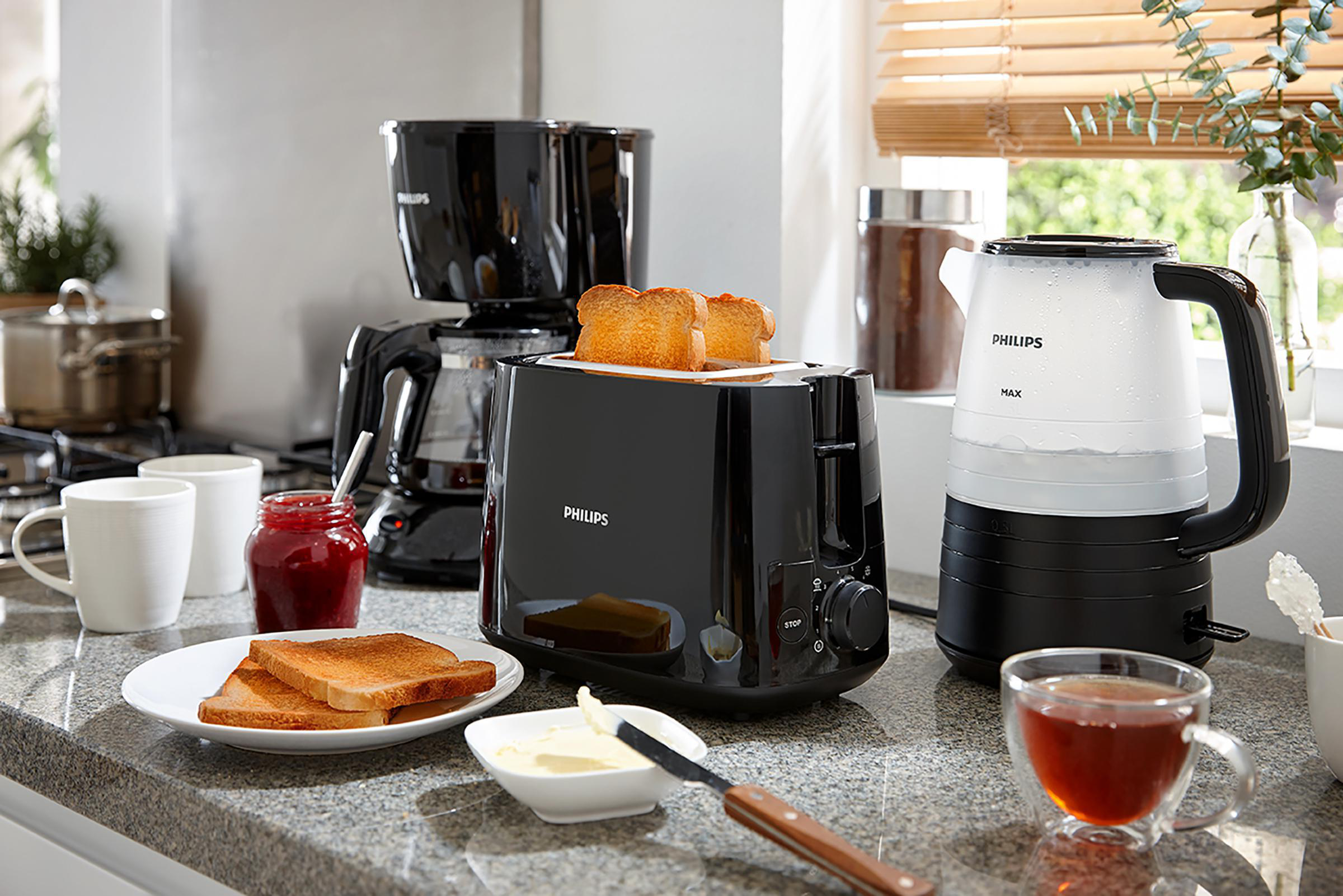 Küchenszene mit Toaster, Kaffeemaschine, Wasserkocher und Frühstücksartikeln auf der Theke.