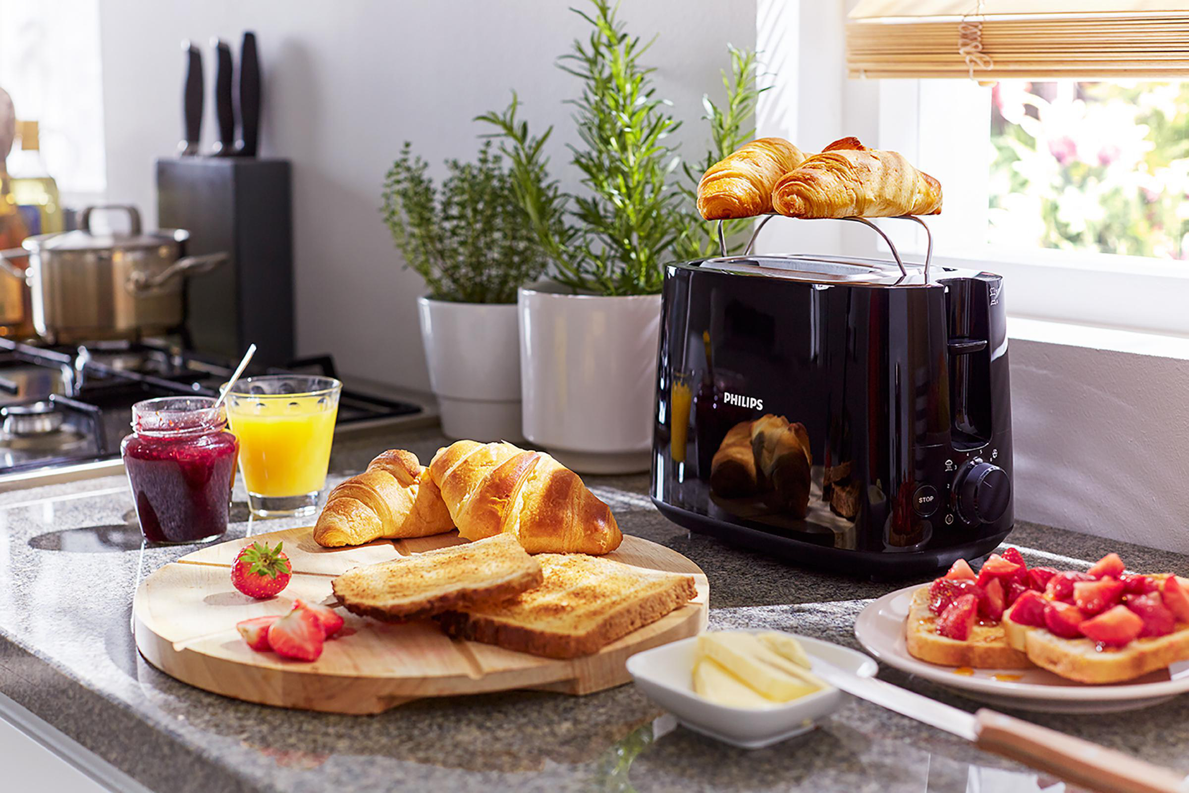 Frühstücksszene: Toaster, Croissants, Toast mit Erdbeeren, Marmelade und Orangensaft. Gemütliche Umgebung.