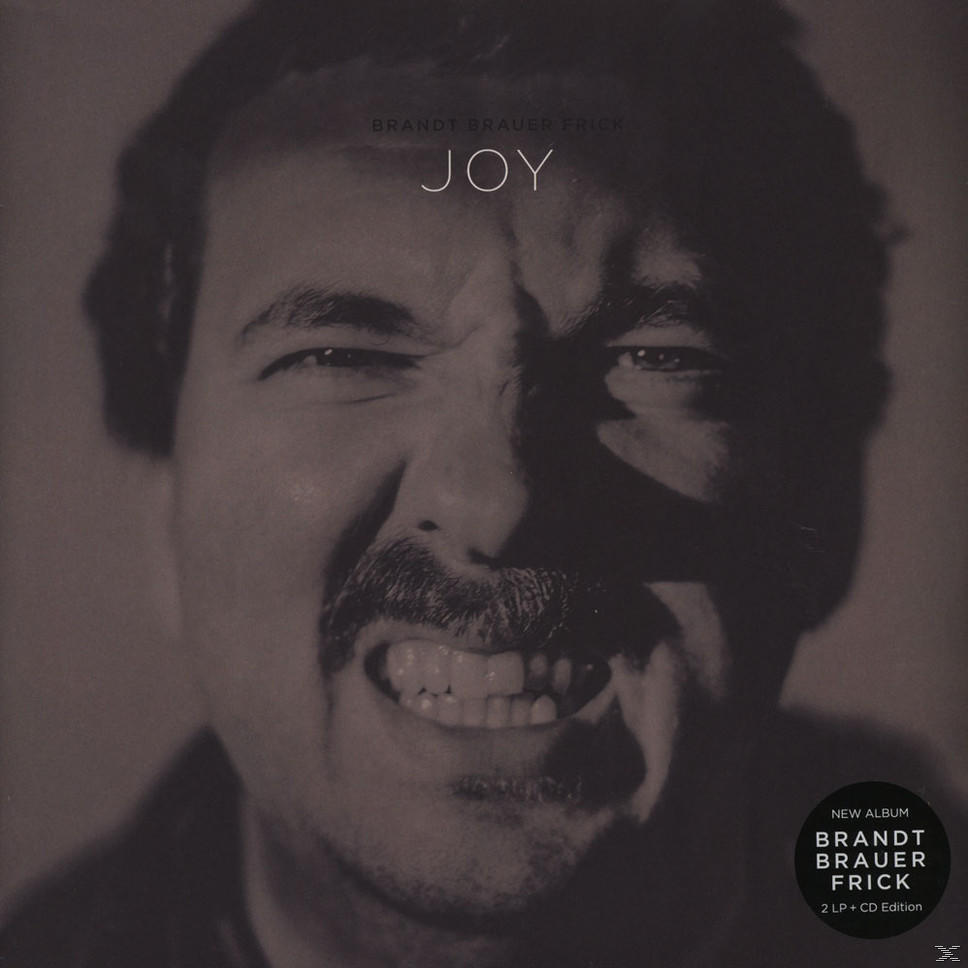 Fekete-fehér album borító. Egy bajuszos férfi grimaszol. A szöveg: 'JOY'.