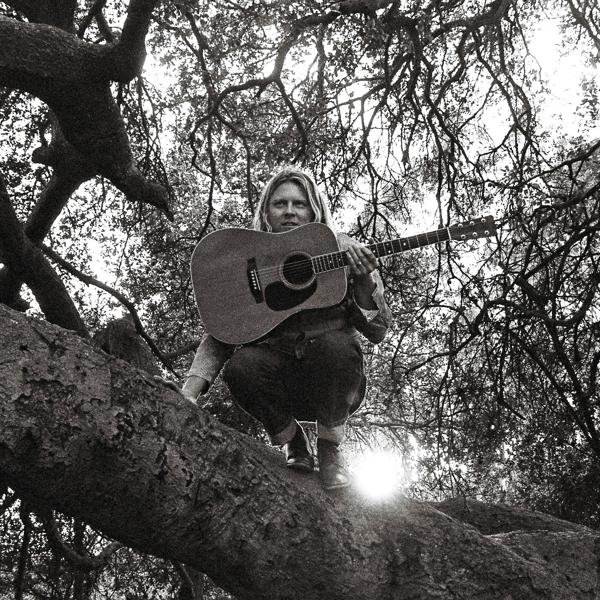 Une femme avec une guitare assise sur une branche d'arbre, en noir et blanc.