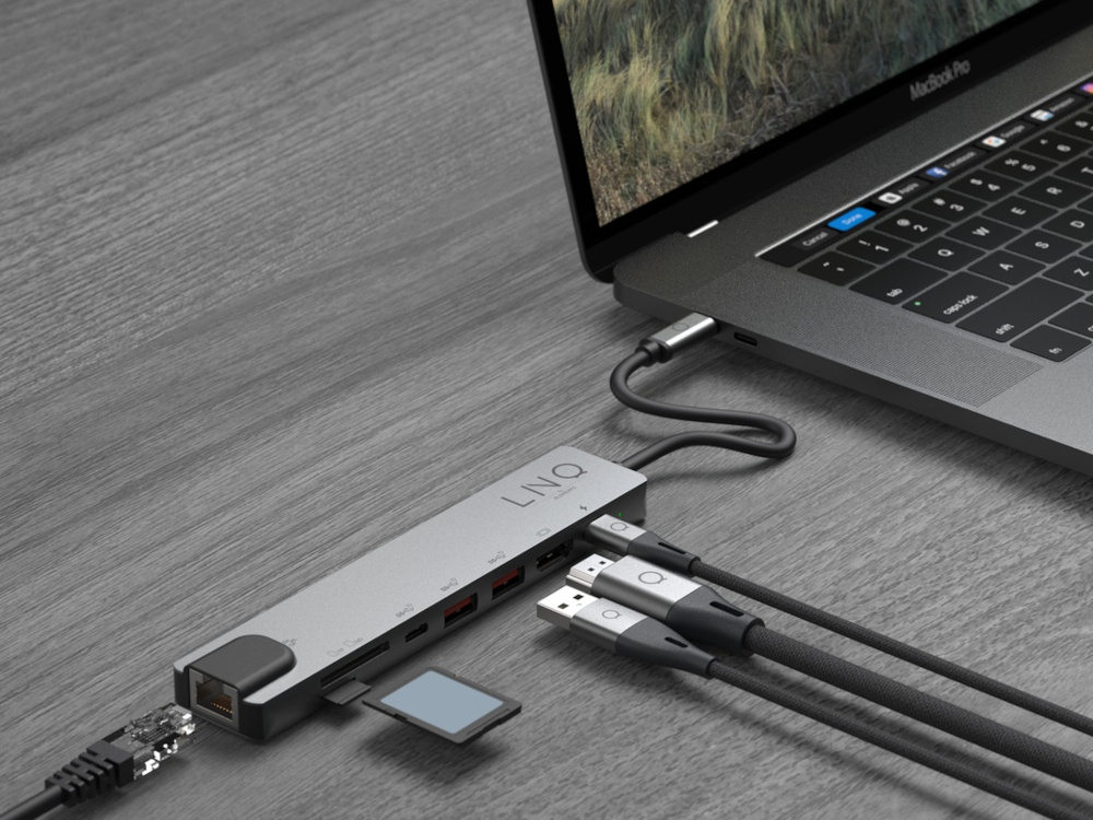 Ordinateur portable avec un hub argenté connecté. Plusieurs câbles sont branchés sur le hub.