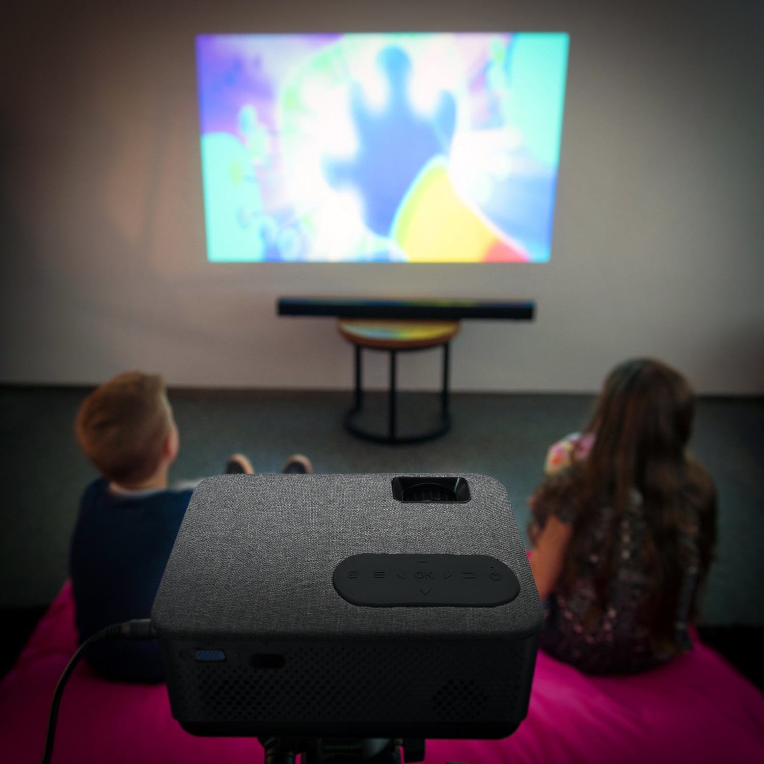 Projecteur affichant un dessin animé. Deux enfants sont assis sur un tapis rose, regardant.