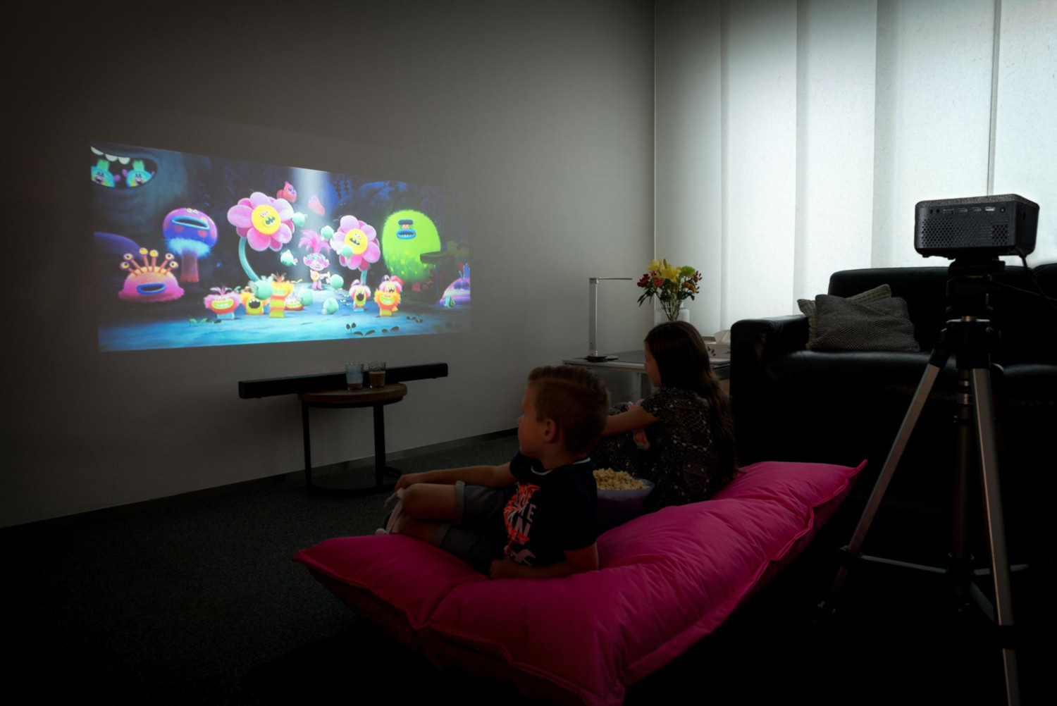 Deux enfants regardant un film projeté sur un mur. Il y a un projecteur et une barre de son dans la pièce.