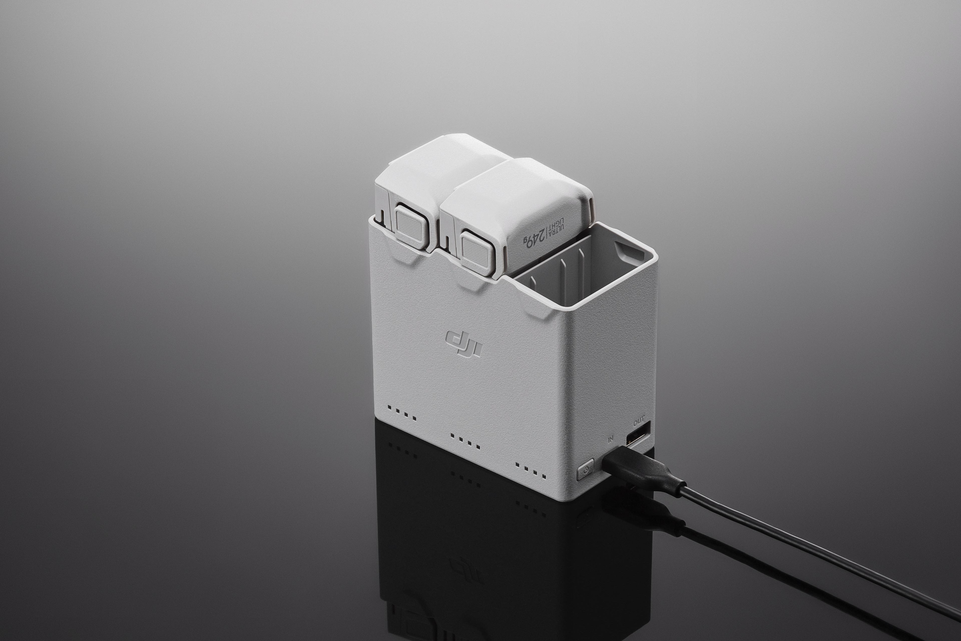 Un chargeur de batterie de drone blanc et gris avec deux batteries à l'intérieur, connecté à un câble de charge noir.