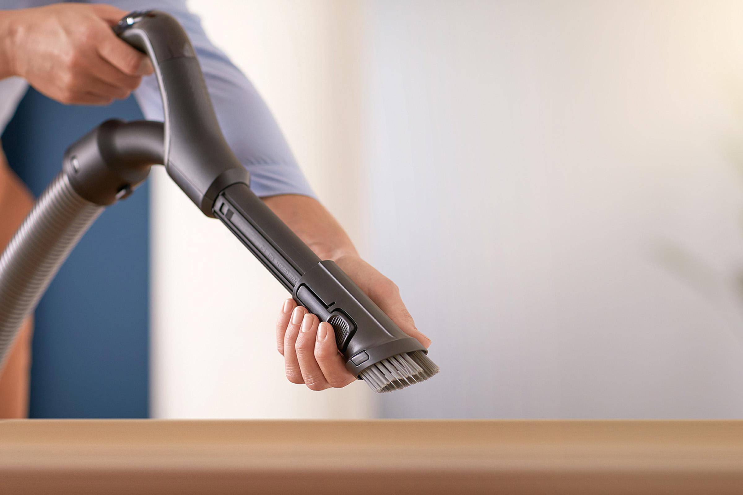 Hände halten Staubsaugeraufsatz über Holzoberfläche.