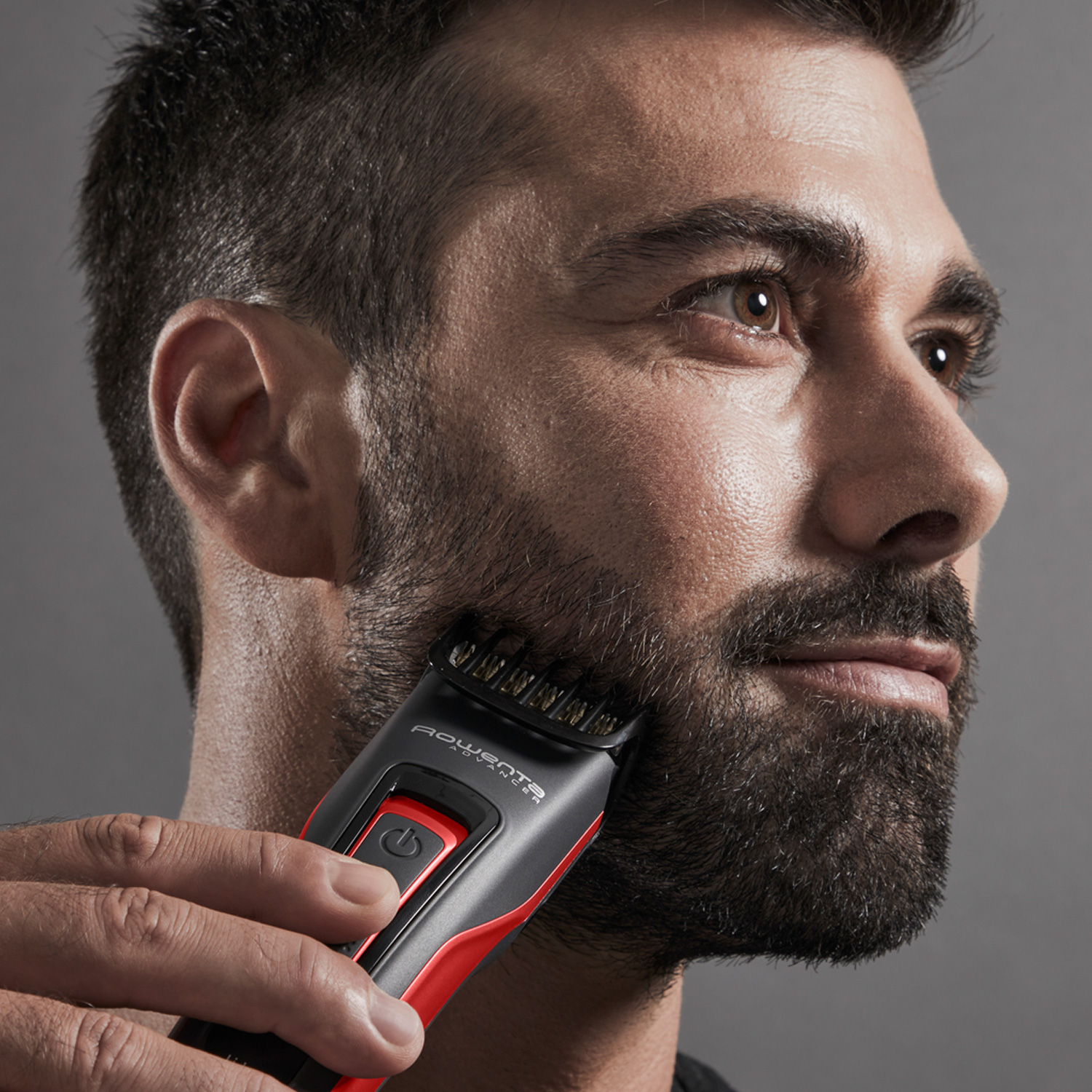 Hombre afeitándose la barba con un recortador de barba negro y rojo.