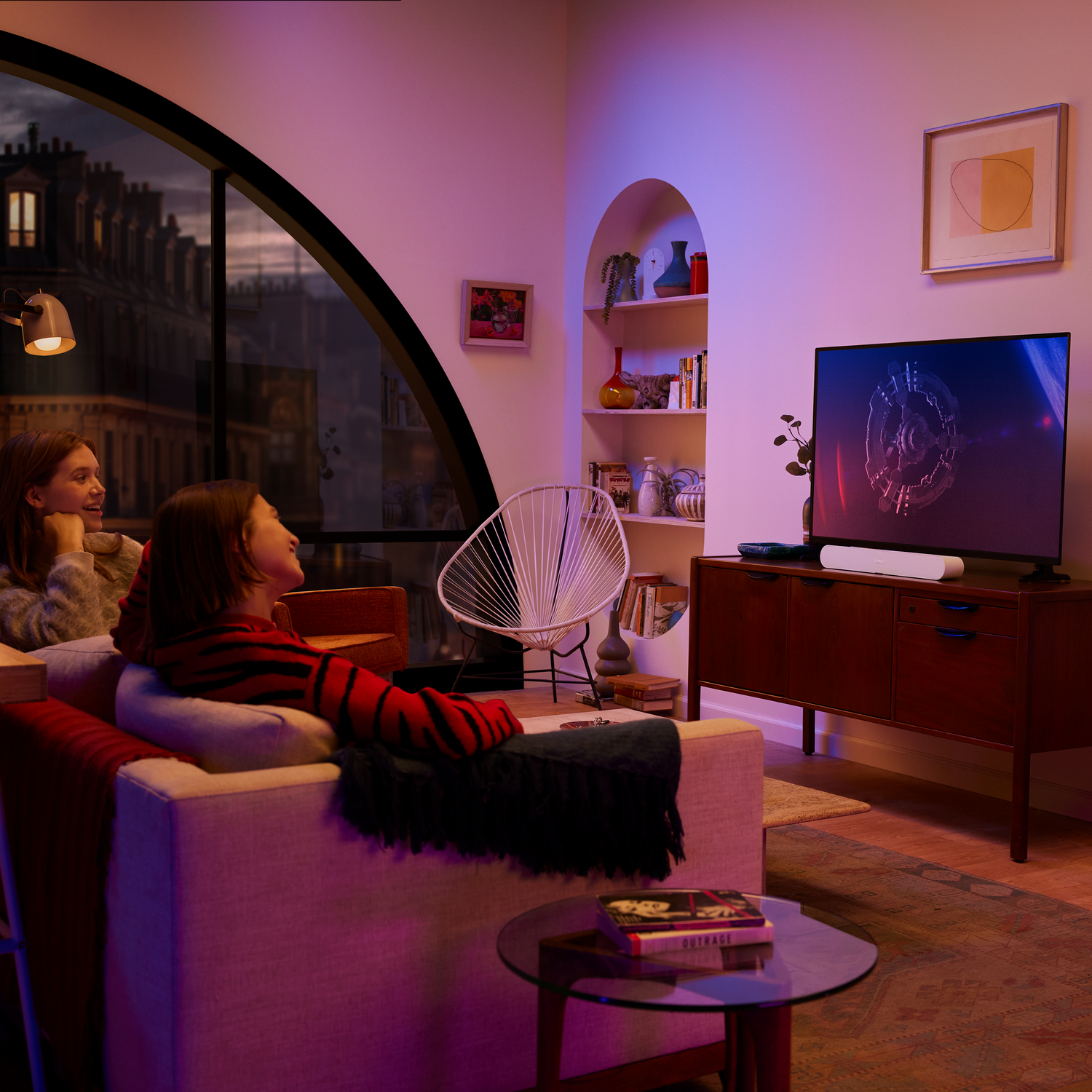 Dos mujeres en un sofá, mirando la pantalla de un televisor en una sala de estar.