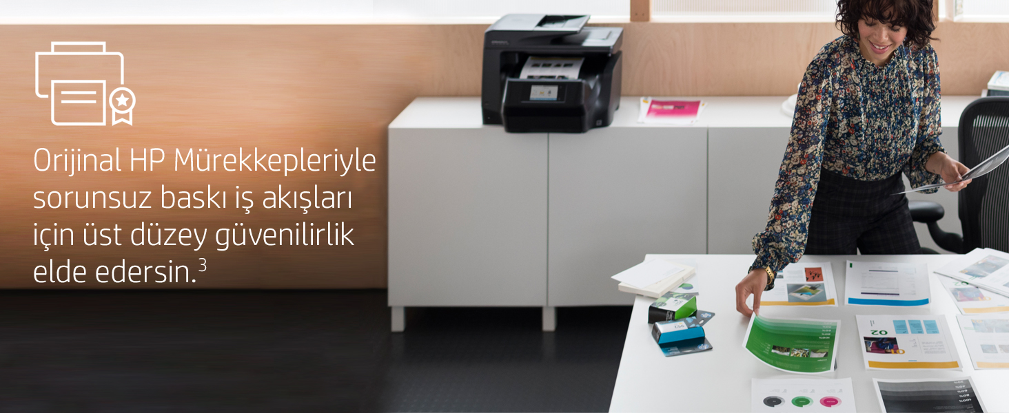 Bir kadın bir yazıcının yanında duruyor, beyaz bir masada kağıtları düzenliyor. Arka planda yazıcı ve masa.