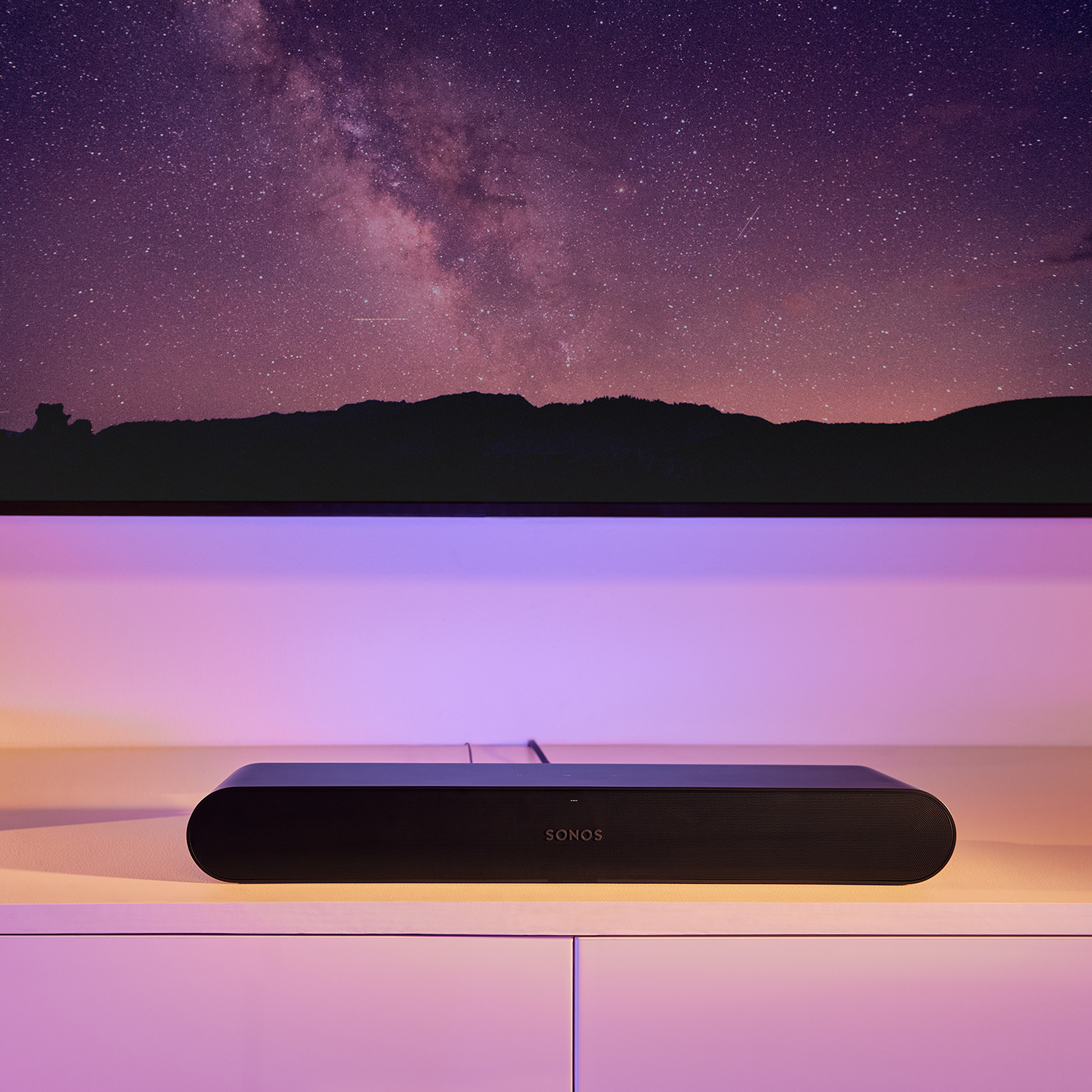 Een zwarte Sonos soundbar op een witte plank met een sterrenhemel erboven.