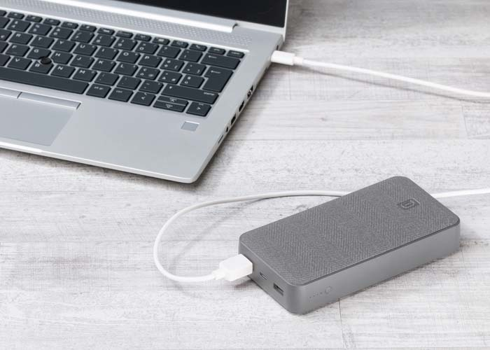 Un ordinateur portable gris est connecté à une batterie externe grise avec un câble blanc.