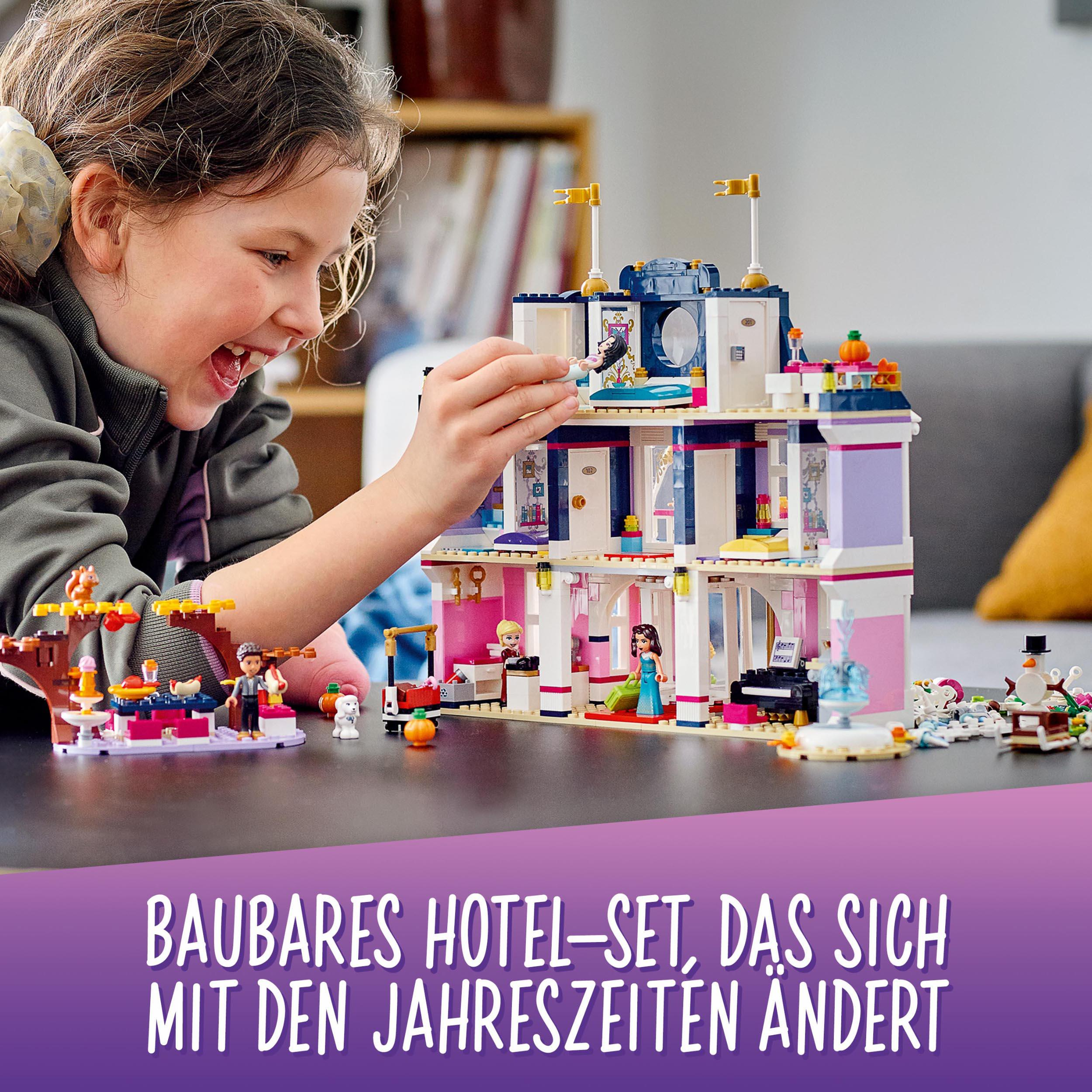 Ein Mädchen lächelt ein Lego-Hotel-Set an. Das Hotel ist mehrstöckig und hat Dekorationen.