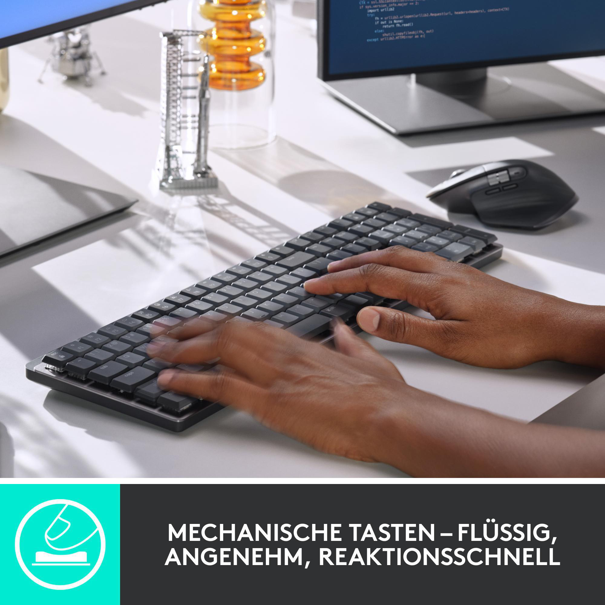 Hände tippen auf schwarzer Tastatur, Maus und Monitor im Hintergrund. Tastatur auf weißem Schreibtisch.