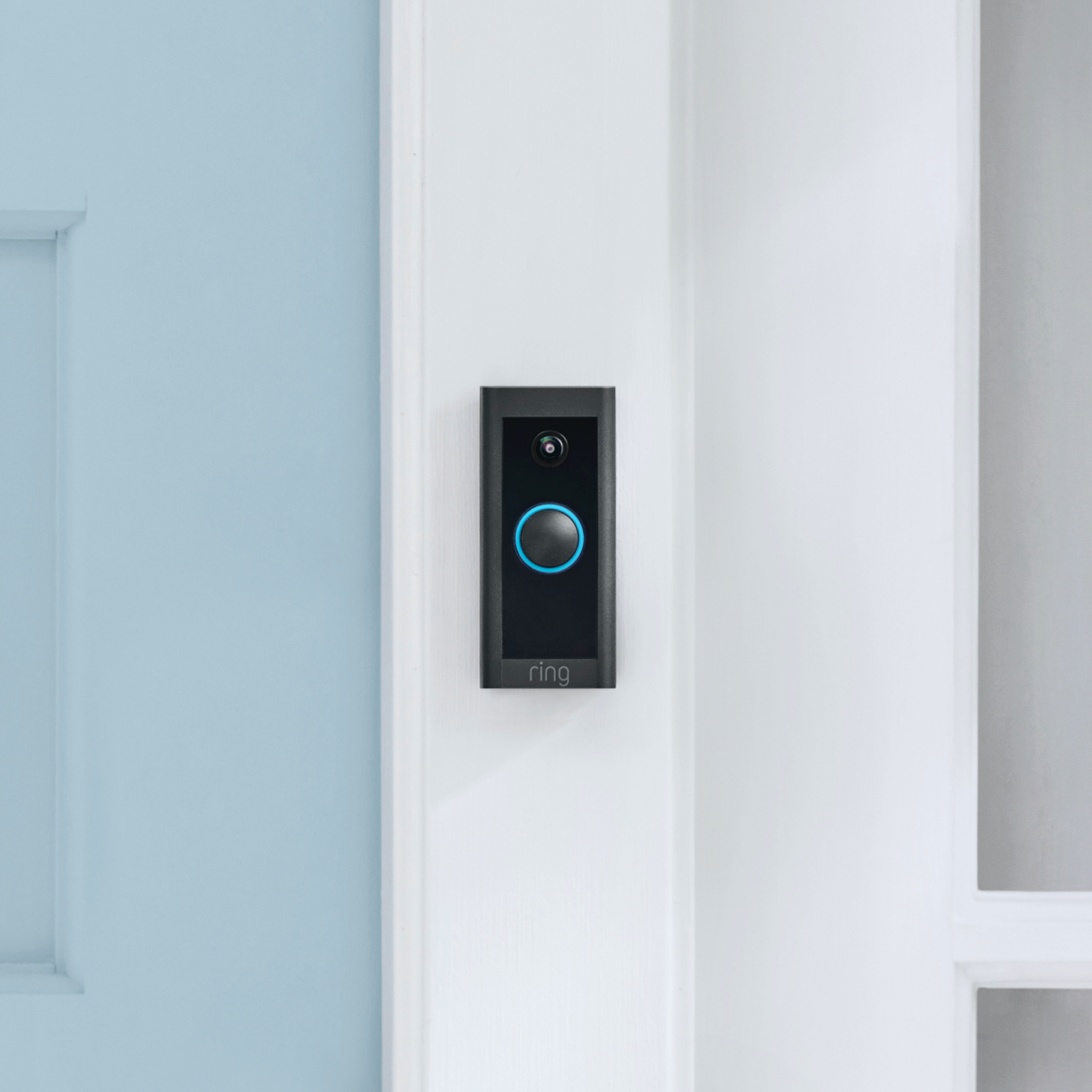 Black Ring video doorbell mounted on a white wall with a blue door.