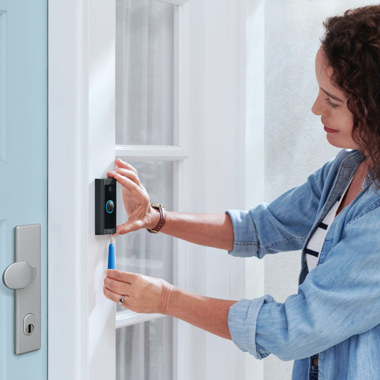 Woman installing a Ring doorbell.  Door is blue, with a white door frame.